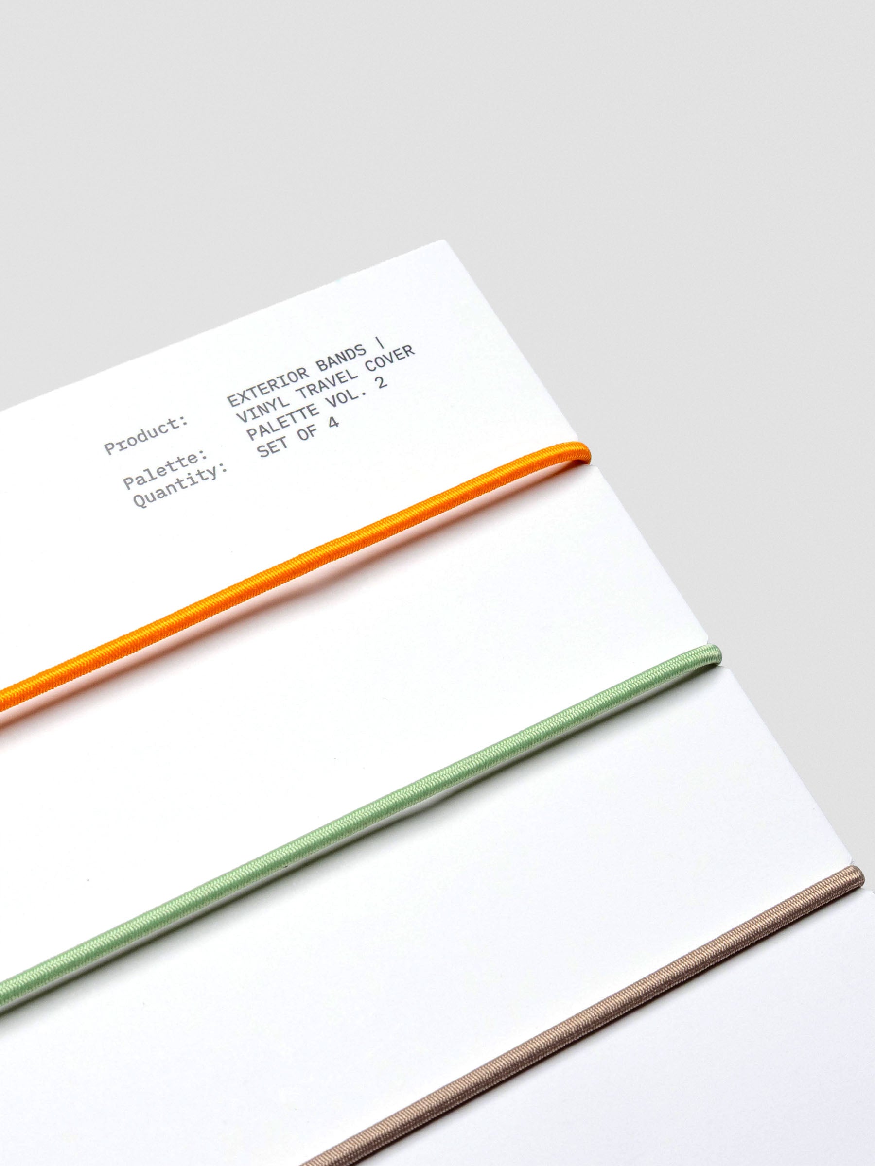 Packaging close-up showing orange, sage, dark brown, and taupe elastic bands.