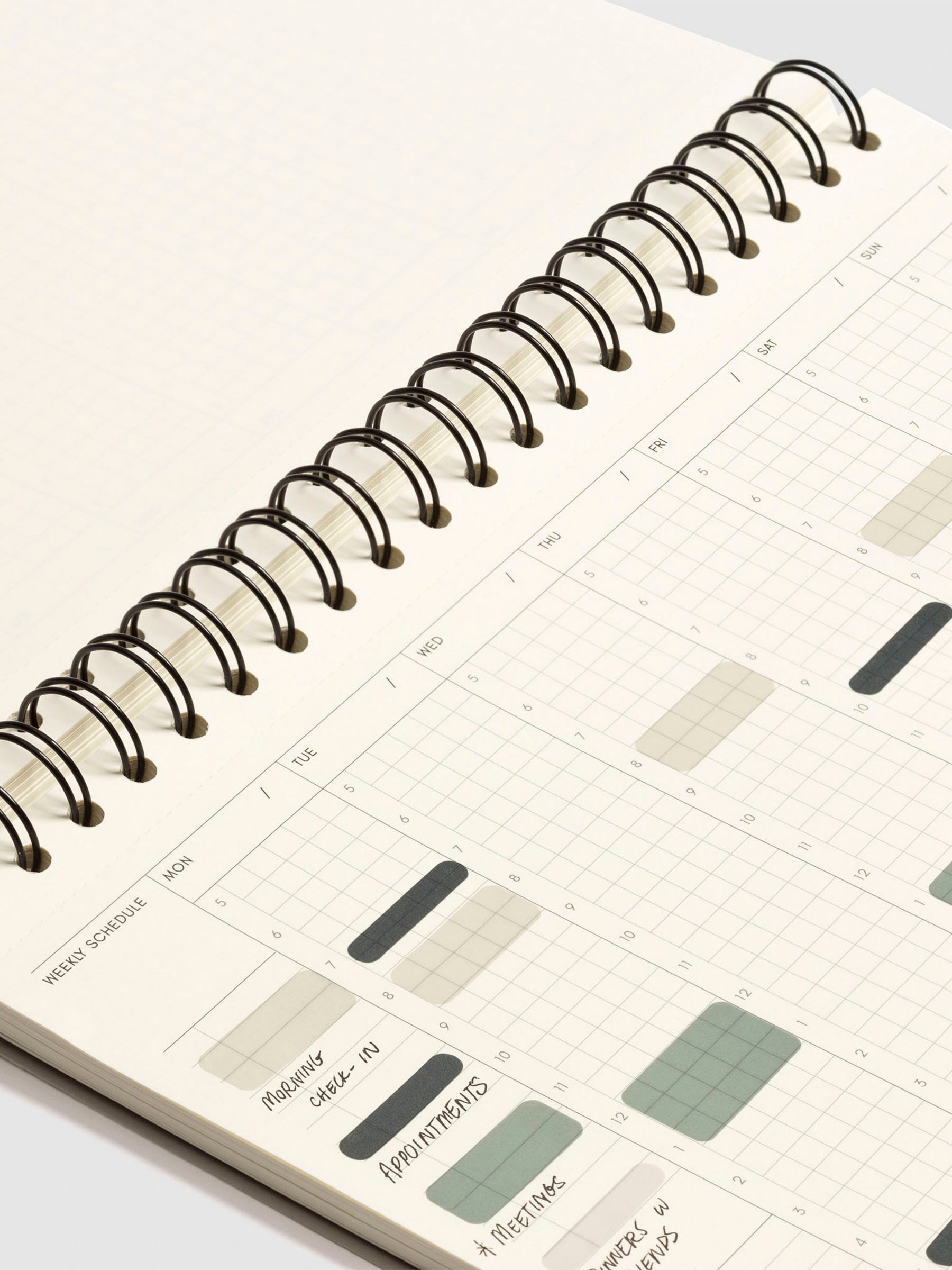 Close up of the spiral binding of the notebook and weekly schedule page. Transparent Time Block stickers are used to block off hours of the day in different colors, and some text has been filled in on the checklist and note fields on the leftmost side of the page.