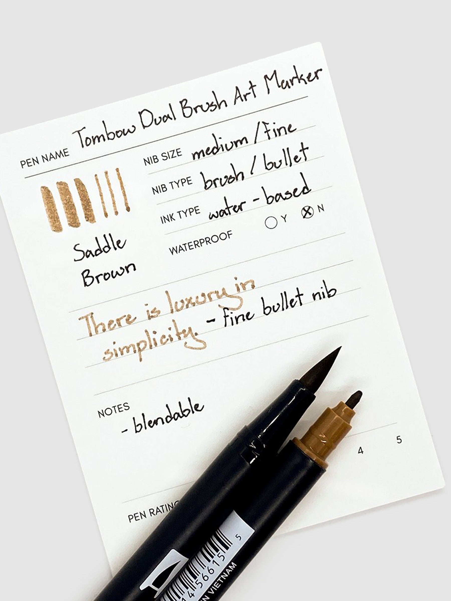 Tombow Dual Brush Art Marker, Saddle Brown, Cloth & Paper. Two Saddle Brown art markers rest with their tips exposed on a pen test sheet.