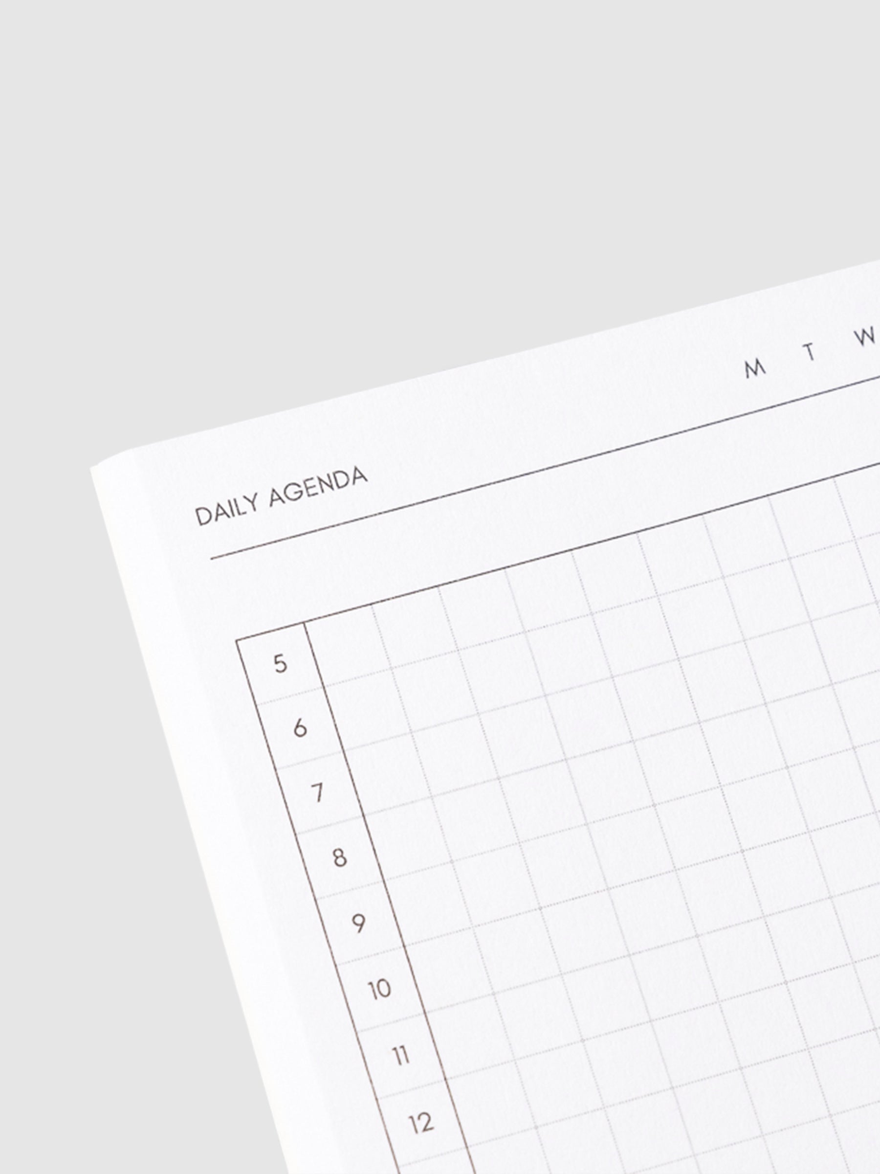 Close up image of the top left corner of the daily agenda notebook page. The page is turned on a left angle and is displayed on a light gray background