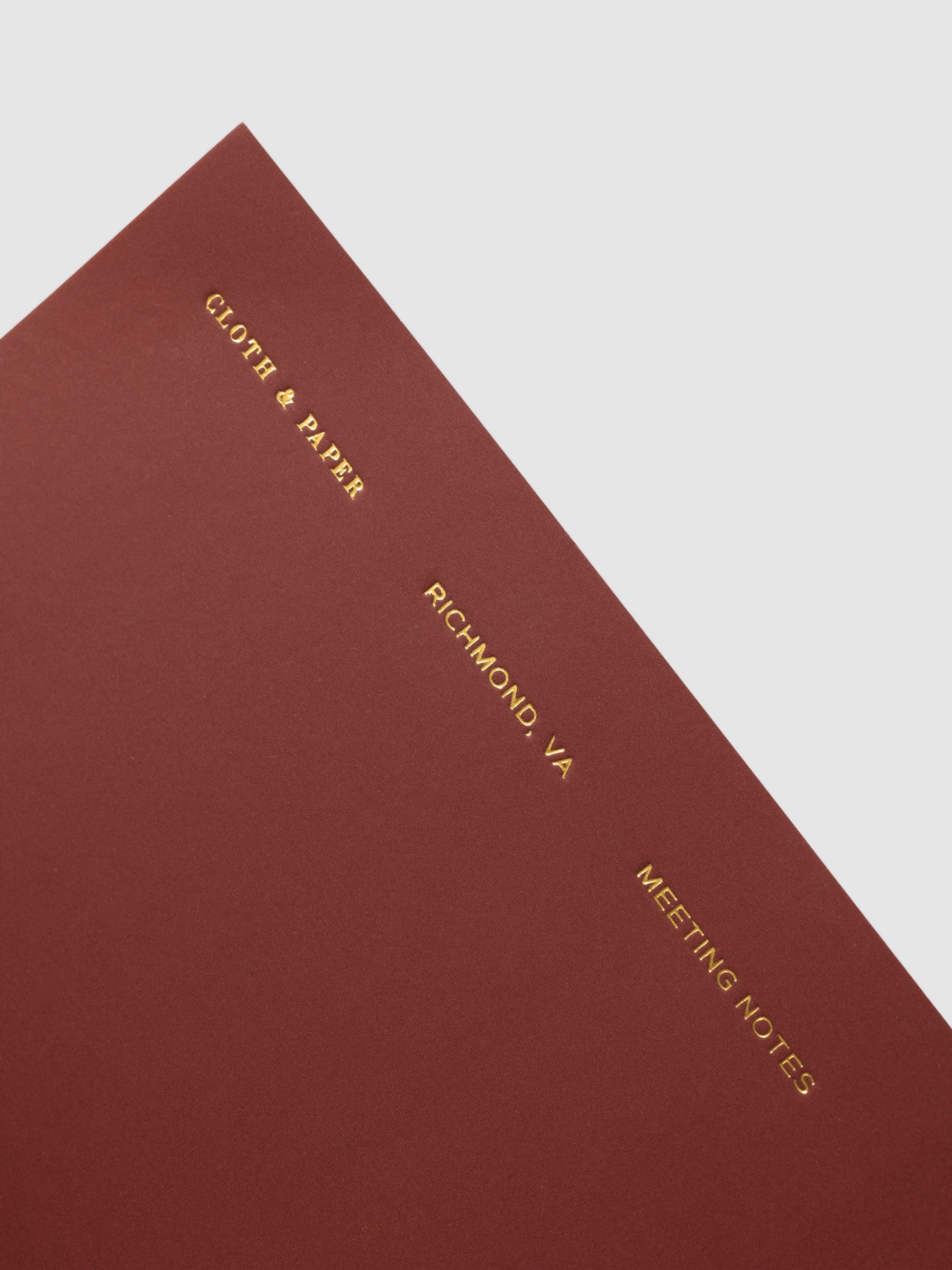 Close up image of the top right of the Meeting Notes Pocket Plus notebook from the Traveler's Notebook Collection. The cover has gold foil text that reads Cloth and Paper Richmond, VA Monthly Admin and is displayed on a neutral background