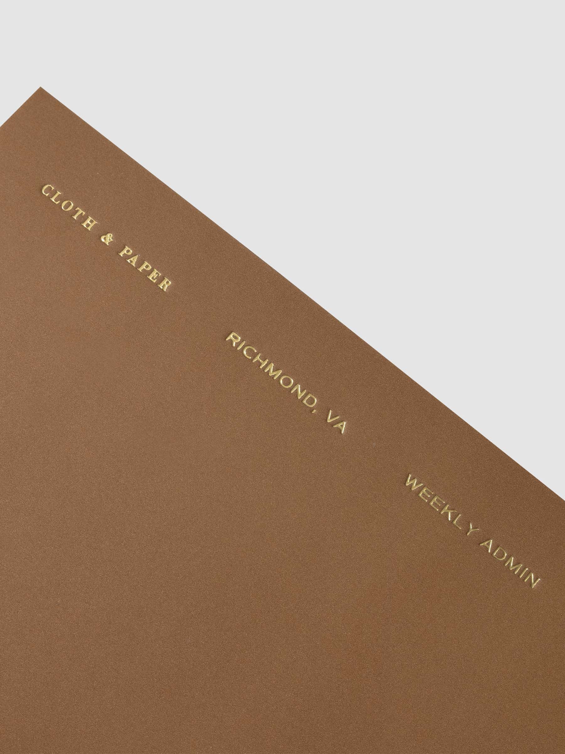 Close up image of the top left of the Weekly Admin Pocket Plus notebook from the Traveler's Notebook Collection. The cover has gold foil text that reads Cloth and Paper Richmond, VA Monthly Admin and is displayed on a neutral background