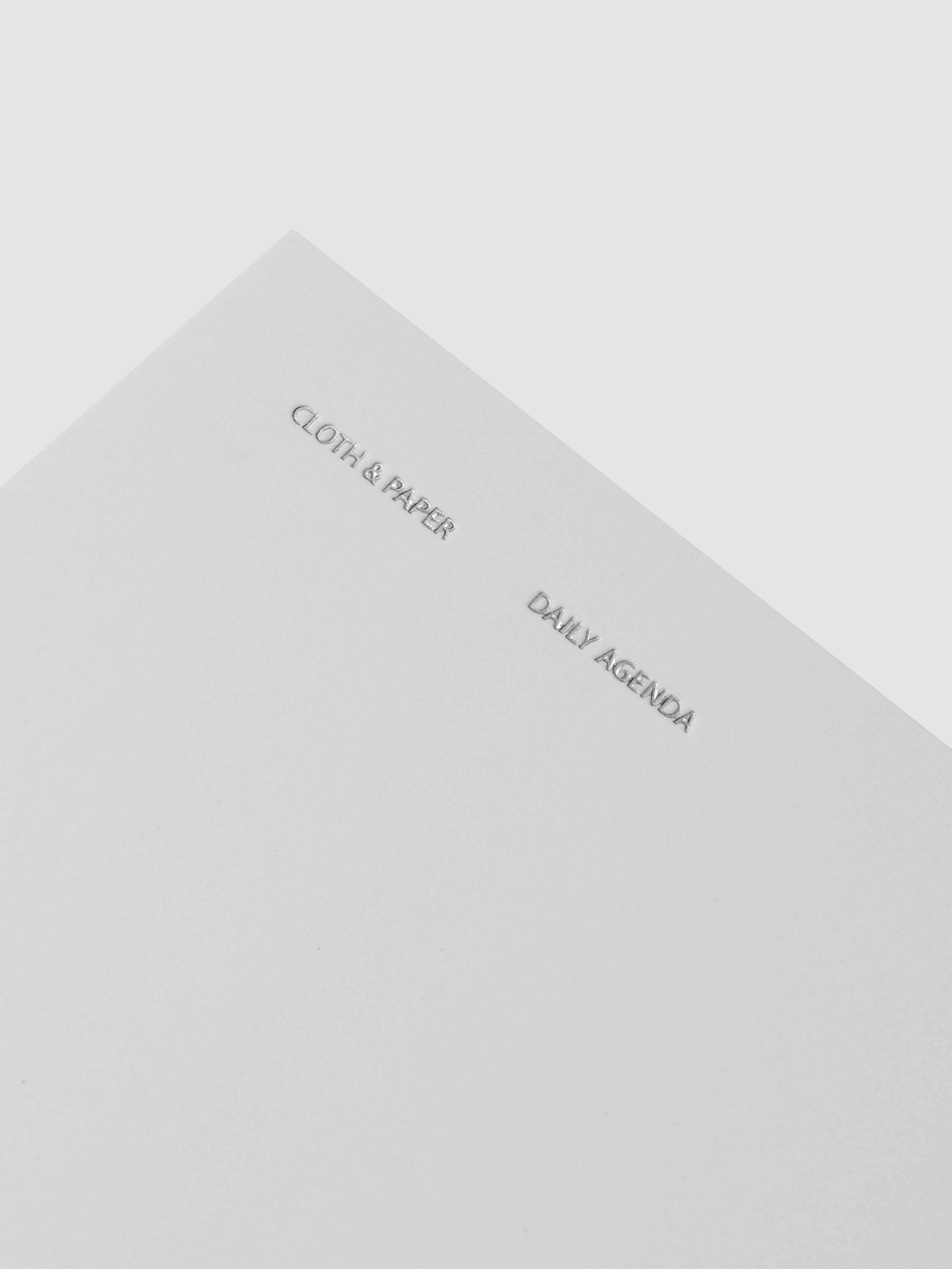 Close up of foil details on Travel Notebook | Pocket Plus | Aspen | Daily Agenda shown closed with packaging against a neutral background.