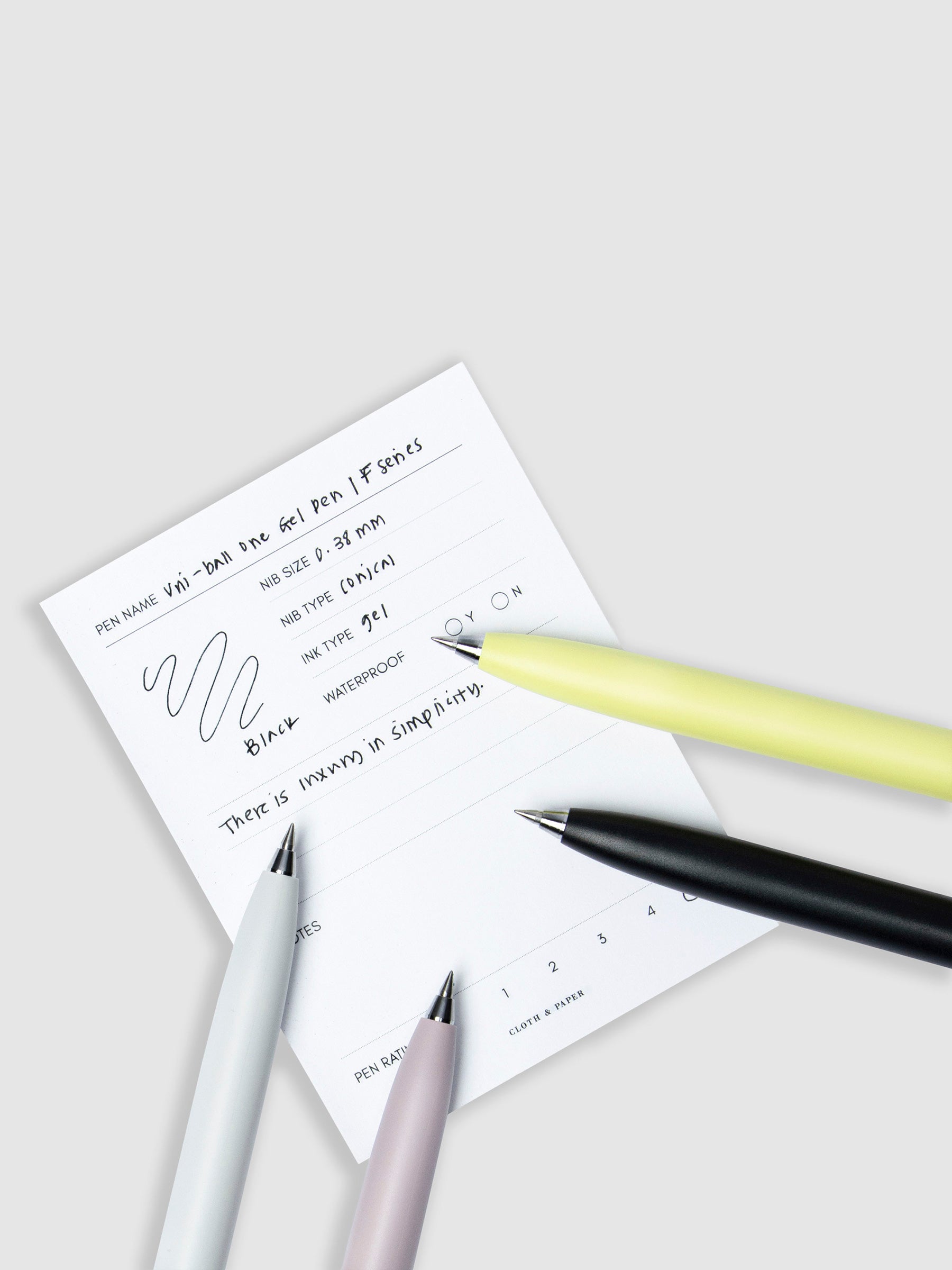 All four pen colors resting on a pen test sheet displaying a writing sample detailing the pen's specs.
