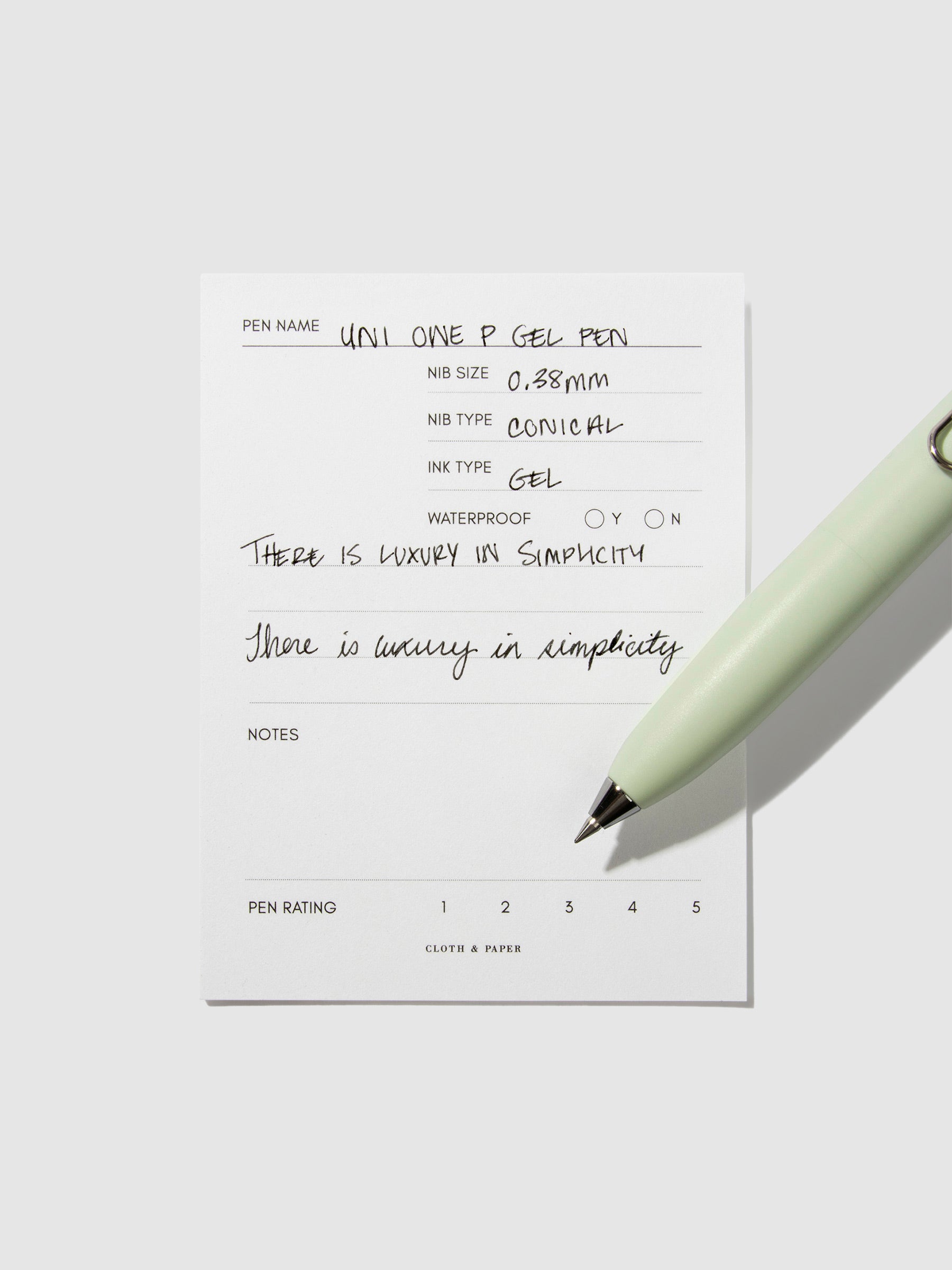 Uni-Ball One P pen resting on a pen test sheet. The sheet shows the pens specs. Color pictured is Mint.