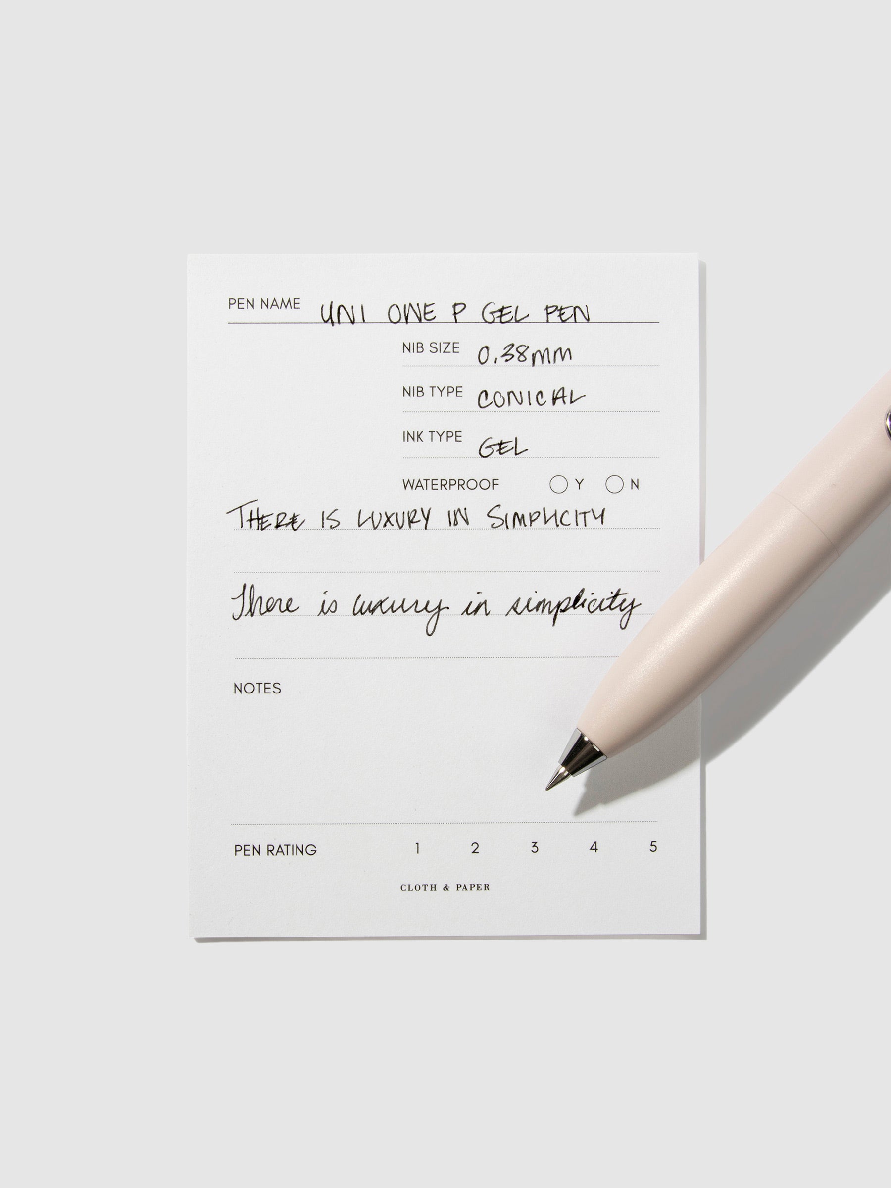 Uni-Ball One P pen resting on a pen test sheet. The sheet shows the pens specs. Color pictured is Peach.