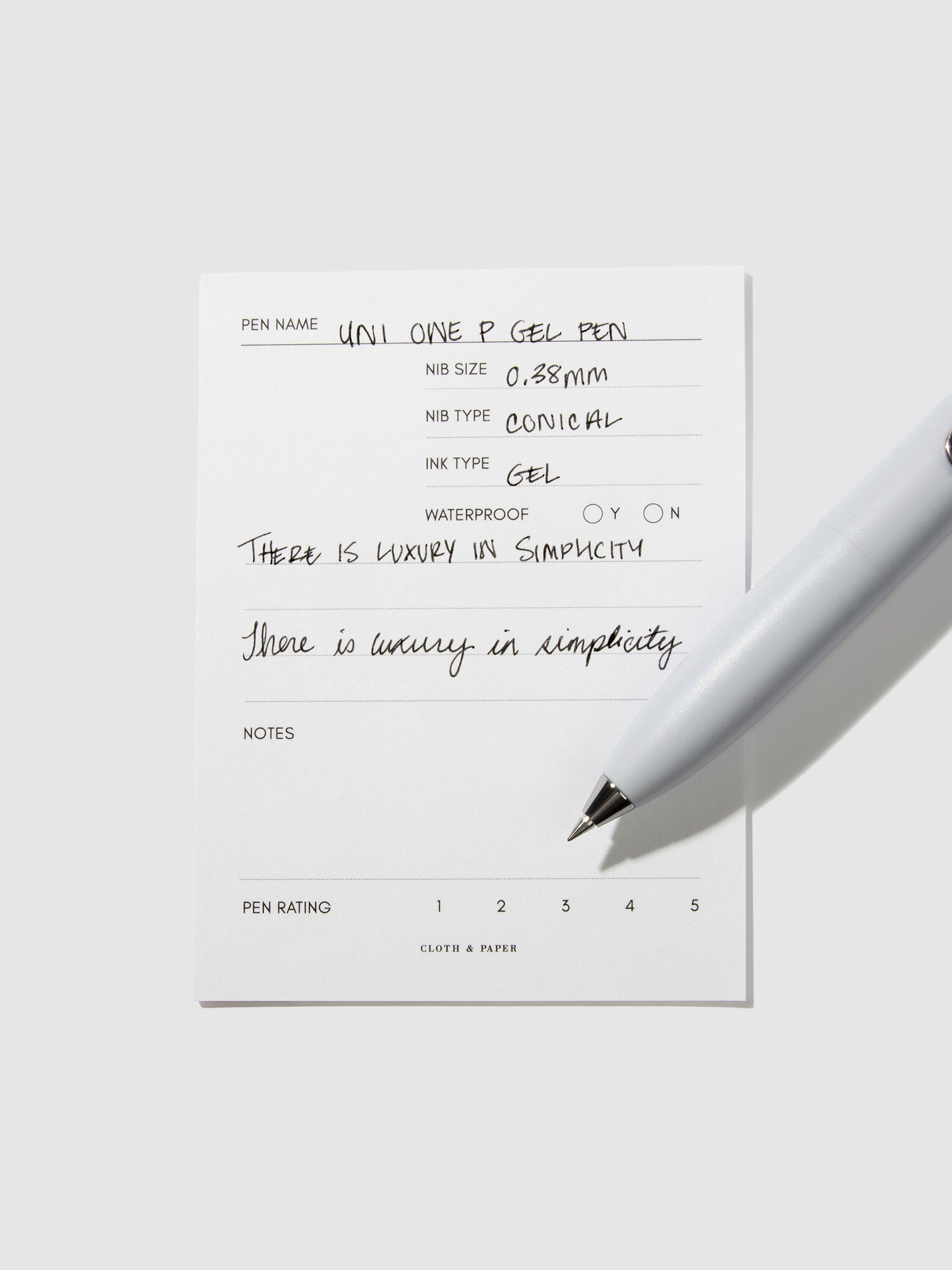 Uni-Ball One P pen resting on a pen test sheet. The sheet shows the pens specs. Color pictured is Soda.