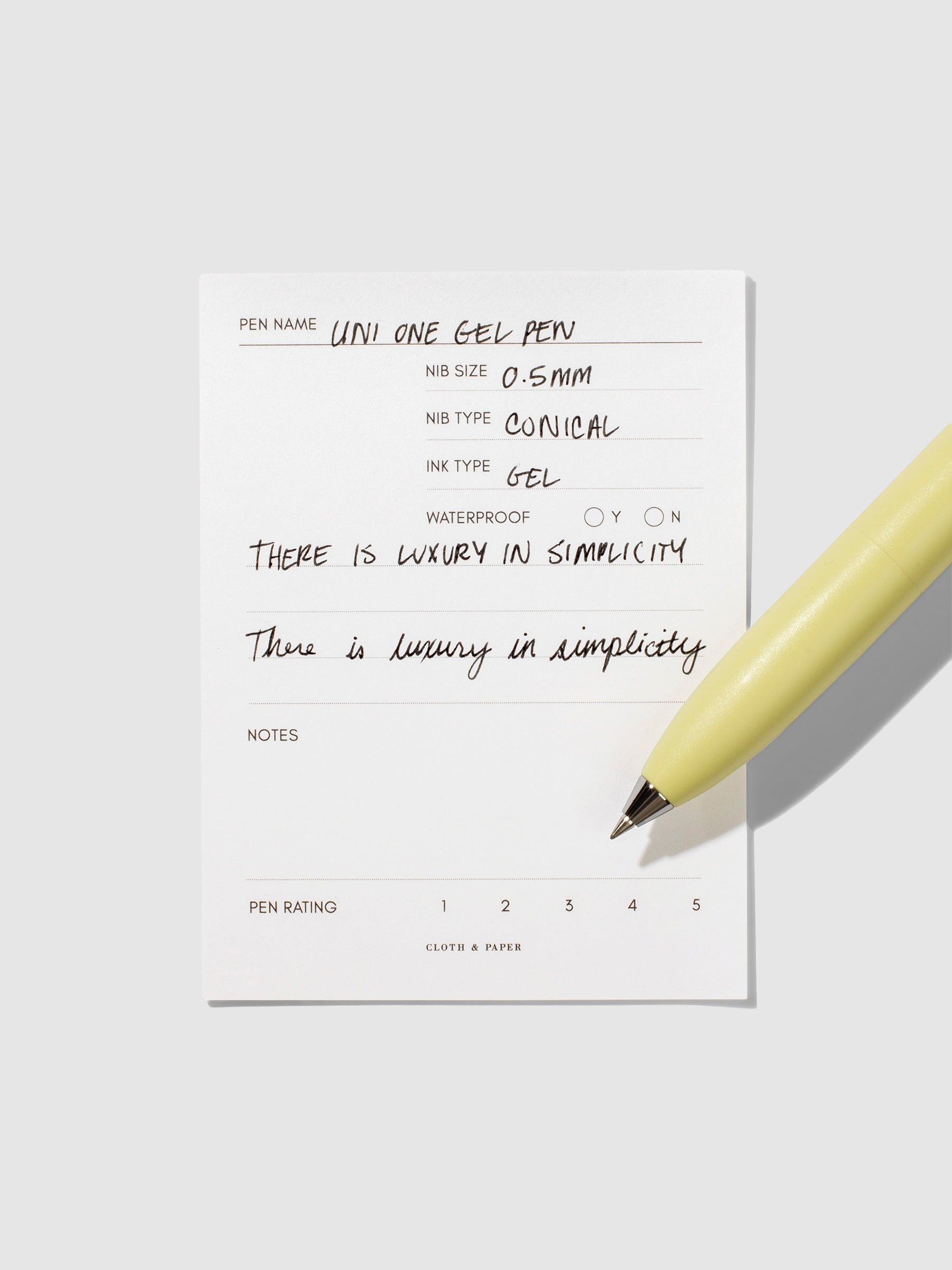 Uni-Ball One P pen resting on a pen test sheet. The sheet shows the pens specs. Color pictured is Banana.