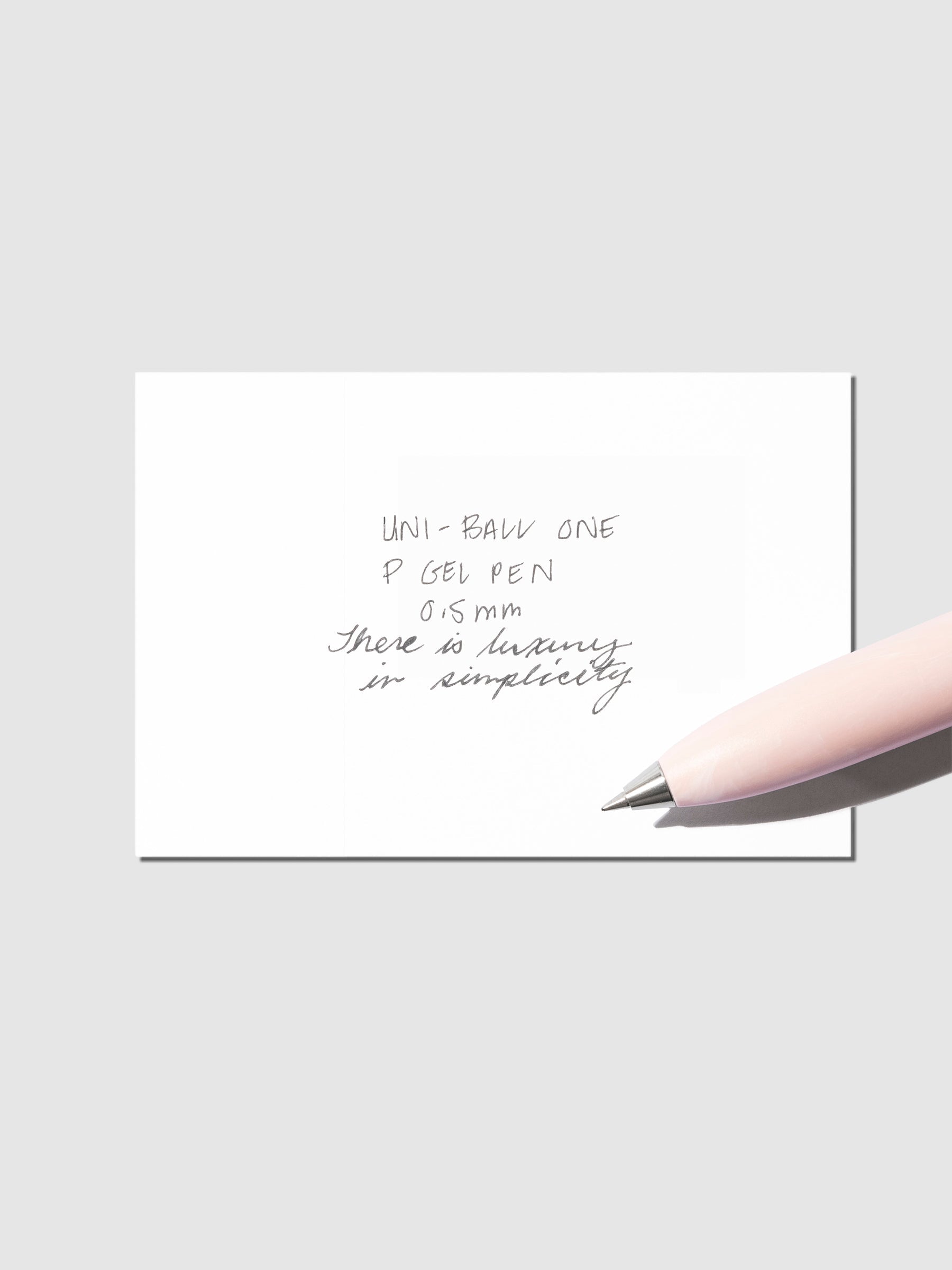 Uni-Ball One P pen resting on a pen test sheet. The sheet shows the pens specs. Color pictured is Peony.