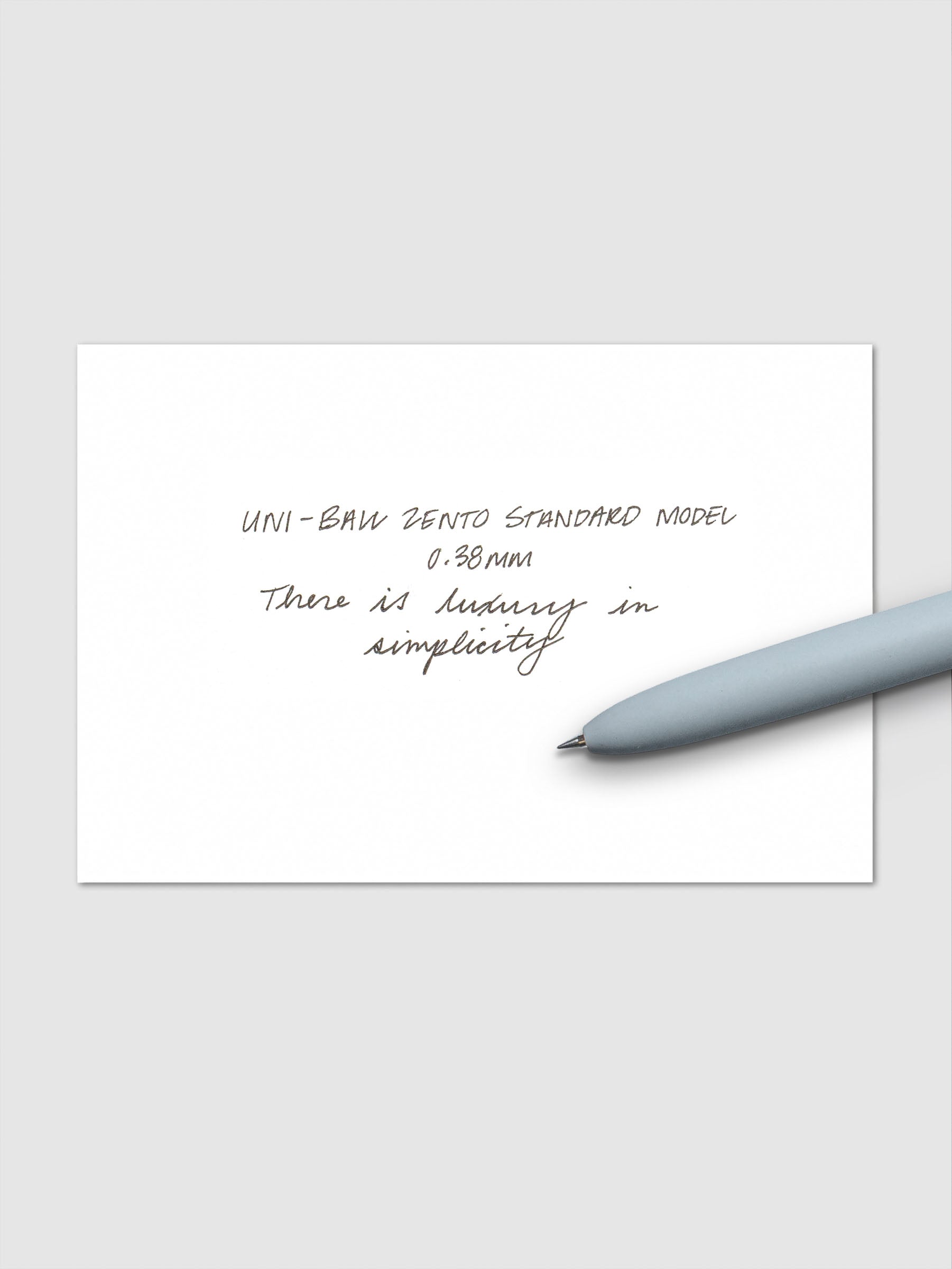 Handwritten sample using the Uni-ball Zento Standard Model Pen with black ink and a 0.38 mm nib. Shown with light blue pen resting across paper.