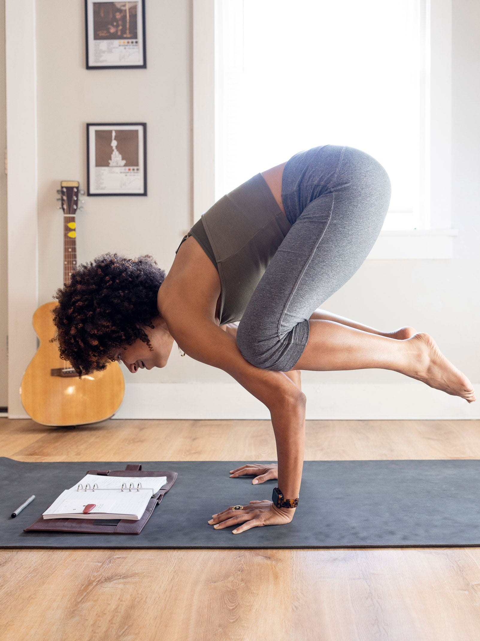 Person practicing yoga on a mat with an opened planner on the mat and a guitar in the background.
