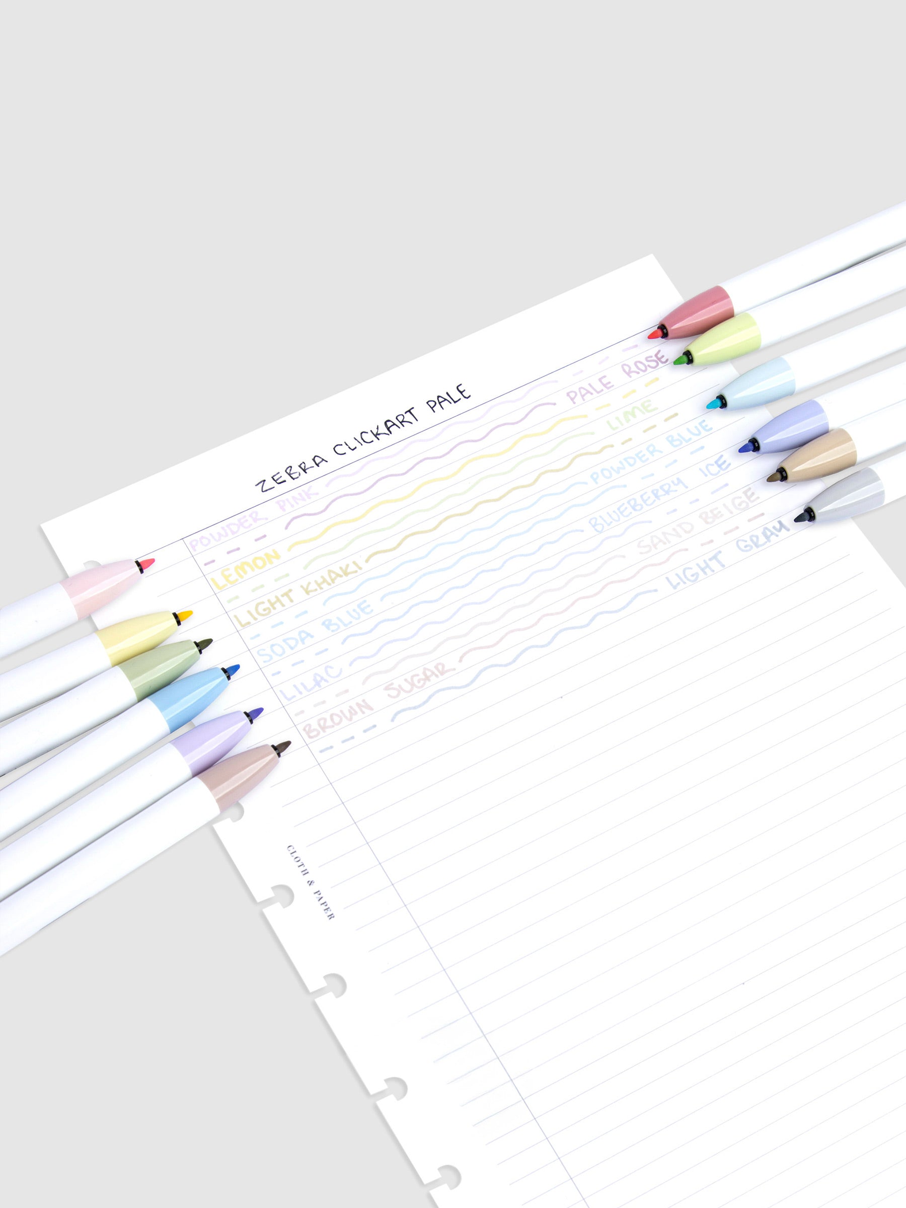 Pen test sheet showing writing and ink color examples of each marker. The 12 markers rest on the left and right edges of the sheet. The colors are Powder Pink, Pale Rose, Lemon, Lime, Light Khaki, Powder Blue, Soda Blue, Blueberry Ice, Lilac, Sand Beige, Brown Sugar, and Light Gray.