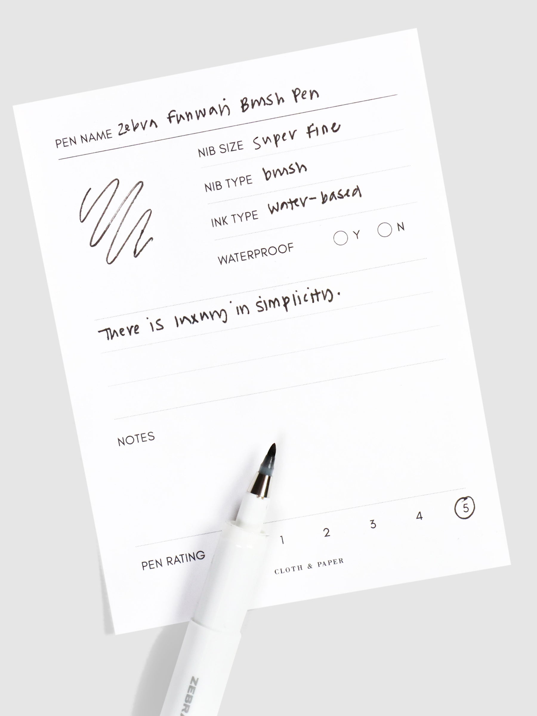 Uncapped end of pen resting on a pen test sheet displaying a writing sample detailing pen specs.