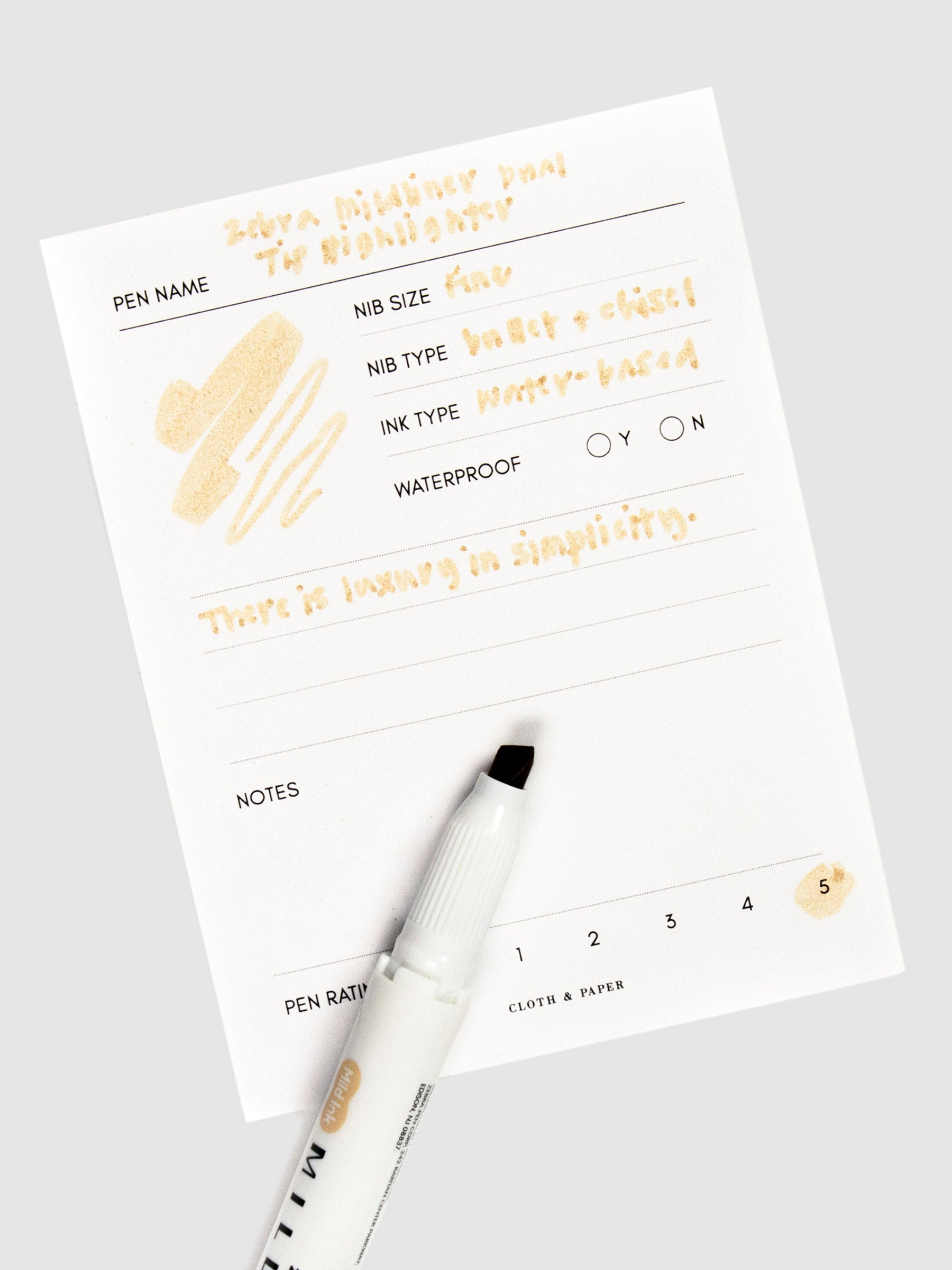 Highlighter in Beige uncapped with felt chisel tip exposed. Highlighter rests on a pen test sheet displaying a writing sample detailing pen specs.