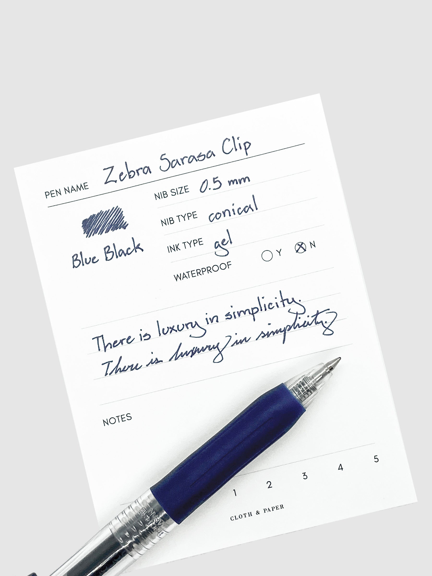 Zebra Sarasa Clip, 0.5 mm, Blue Black, Cloth and Paper. Pen resting on pen test sheet displaying writing sample.