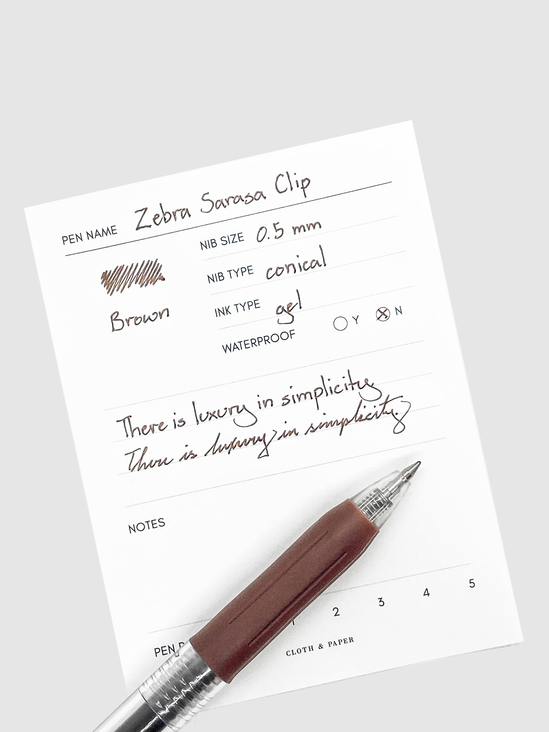 Zebra Sarasa Clip, 0.5 mm, Brown, Cloth and Paper. Pen resting on pen test sheet displaying writing sample.