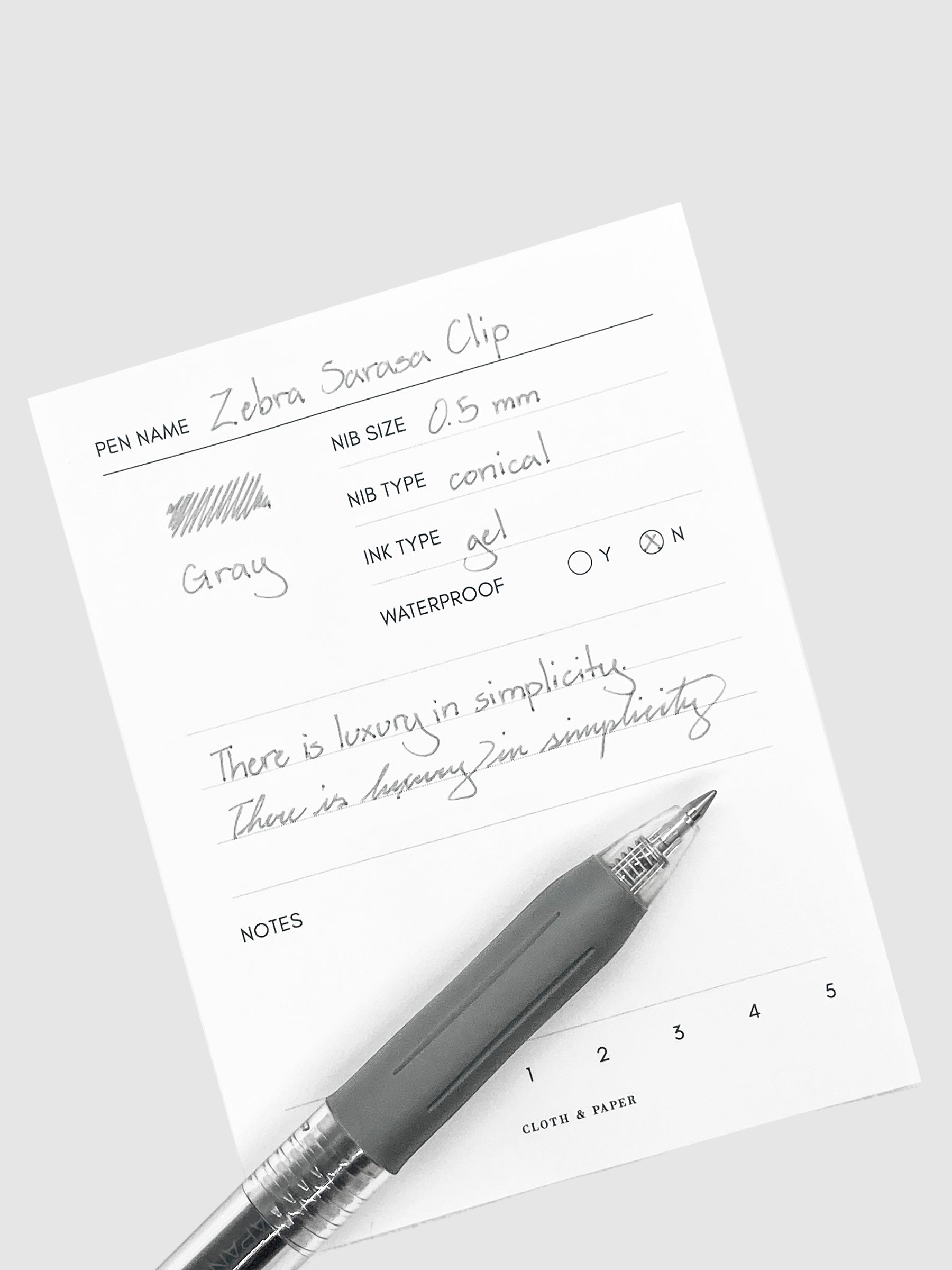 Zebra Sarasa Clip, 0.5 mm, Gray, Cloth and Paper. Pen resting on pen test sheet displaying writing sample.