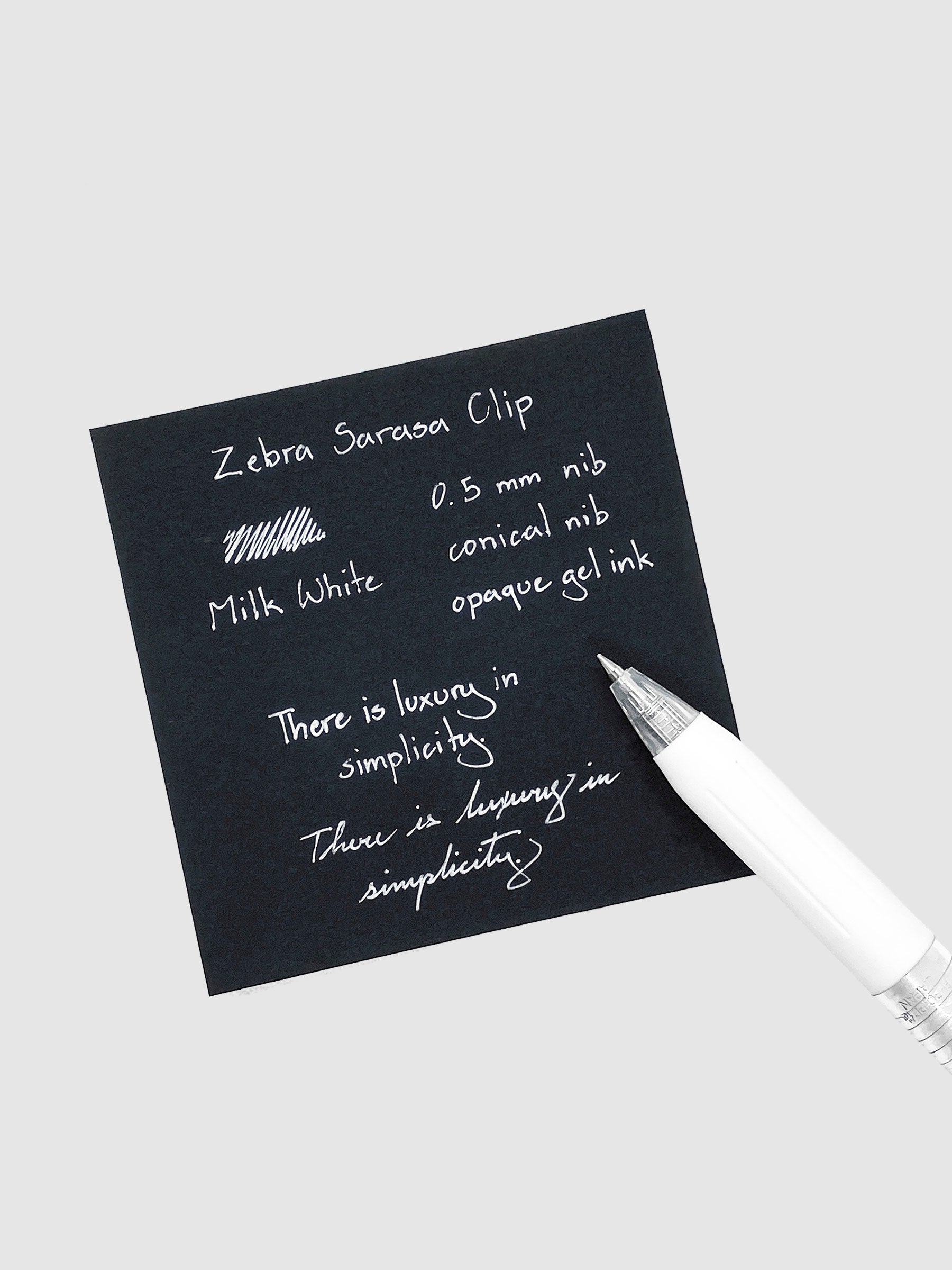 Zebra Sarasa Clip, 0.5 mm, Milk White, Cloth and Paper. Pen resting on black paper displaying writing sample.