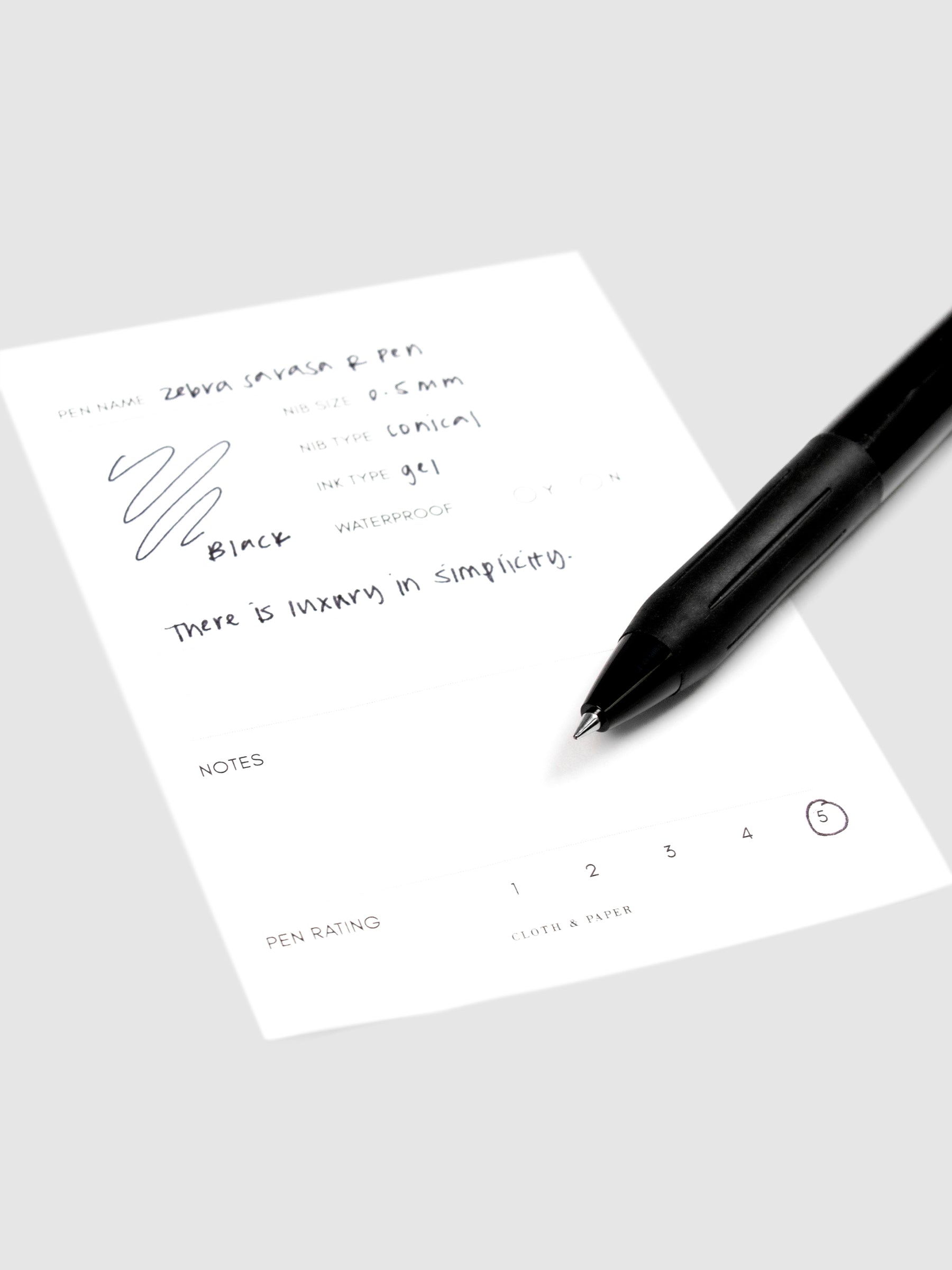 Zebra Sarasa R Pen, 0.5 mm, Black Ink, Black Body, Cloth and Paper. Close up on pen nib resting on pen test sheet.