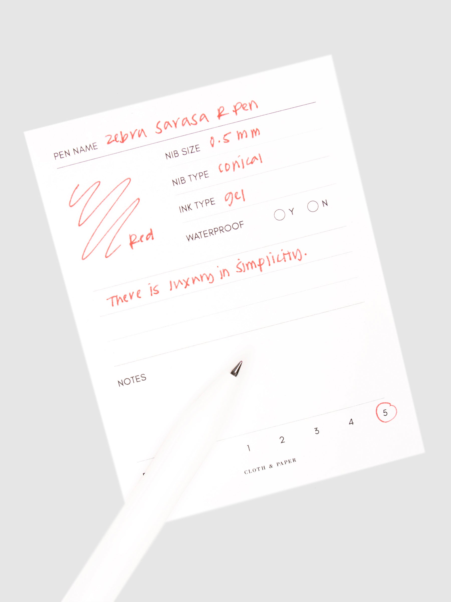 Zebra Sarasa R Pen, 0.5 mm, Red, Cloth and Paper. Pen resting on pen test sheet displaying writing sample.