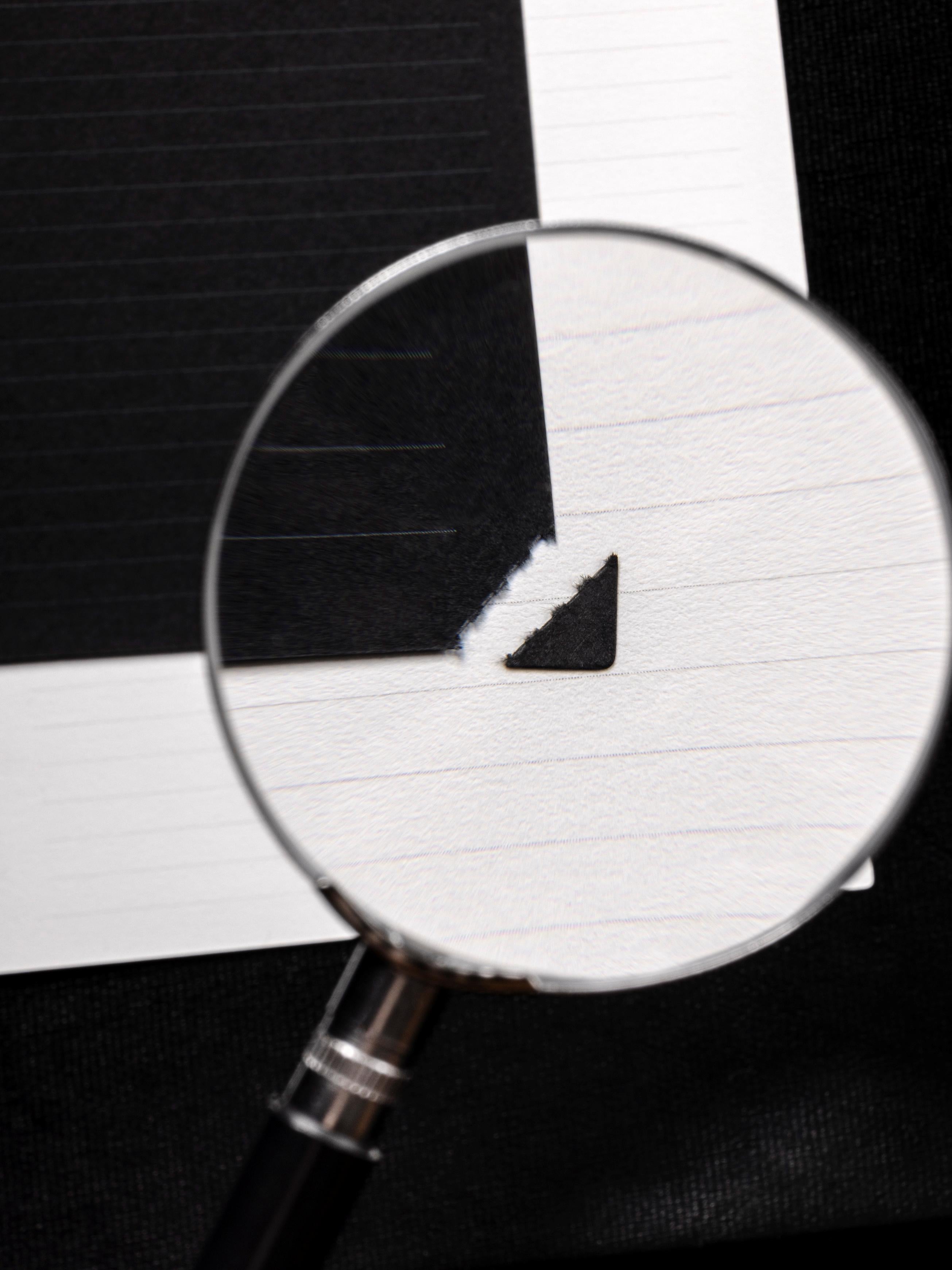 A close-up shot of the torn, perforated edge of a black Lined Planner Inserts from the April Intention Box, shown through a magnifying glass.