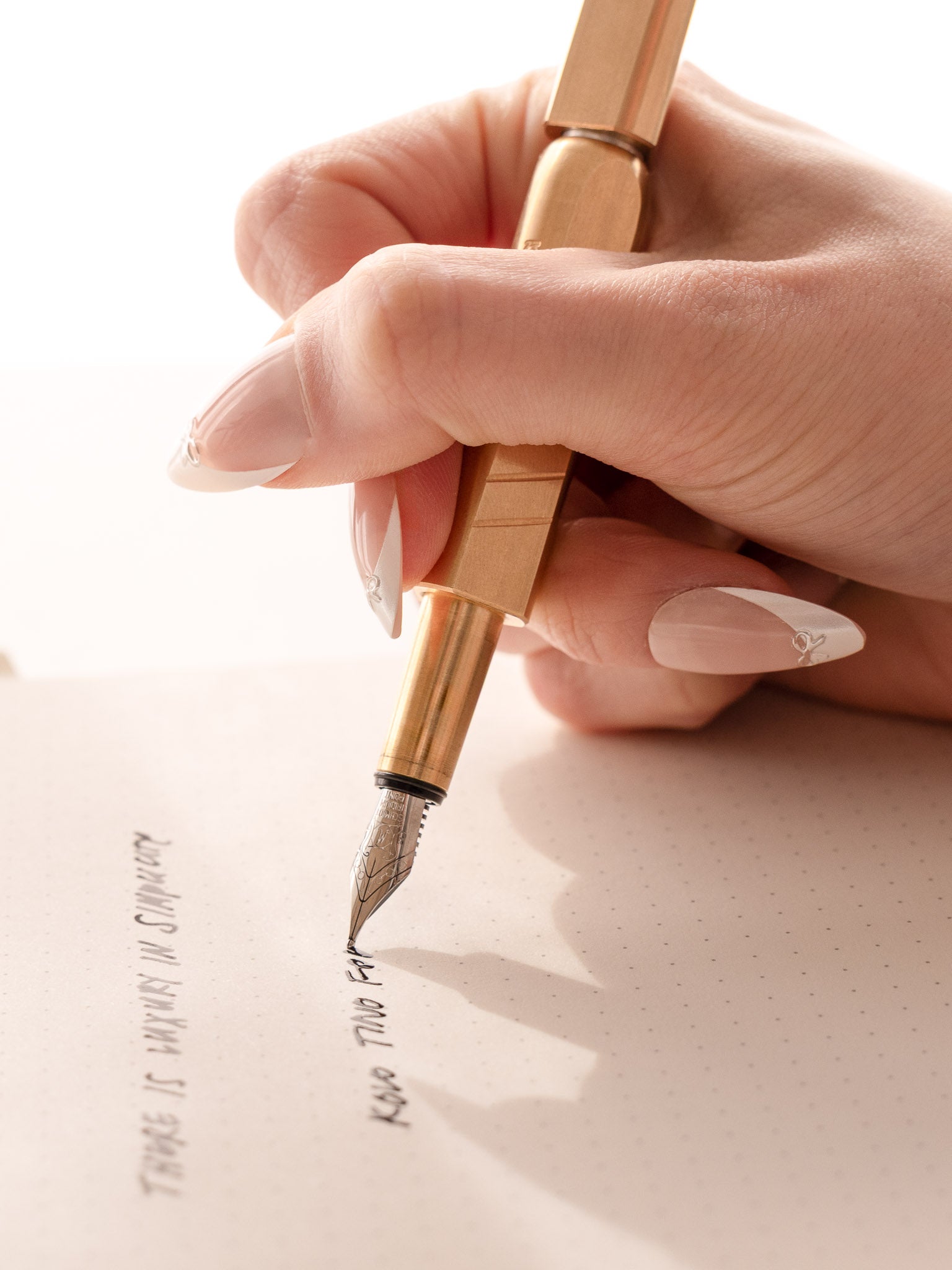 A hand writing on paper with the Kolo Tino Fountain pen in raw brass.