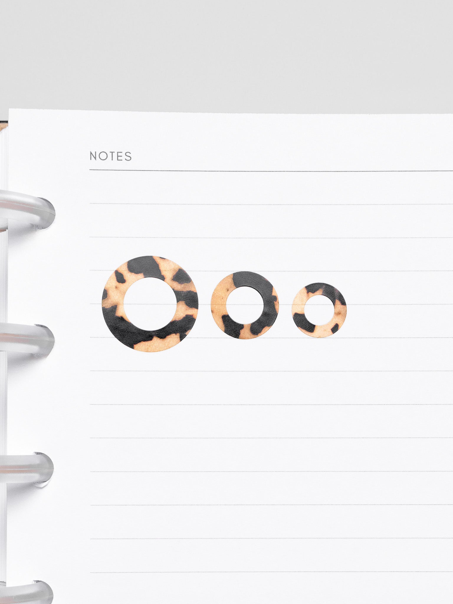 One of each size of the Spotlight Stickers in the pattern Desert Tortoiseshell on a lined notes planner insert.