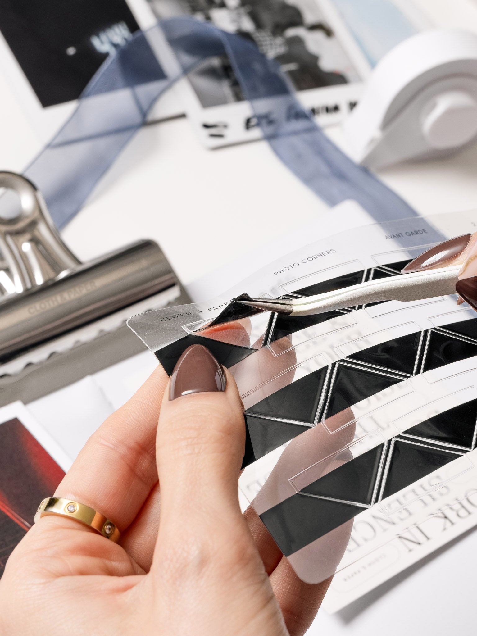 Hands holding a sheet of Photo Corner Stickers peeling one off with tweezers.