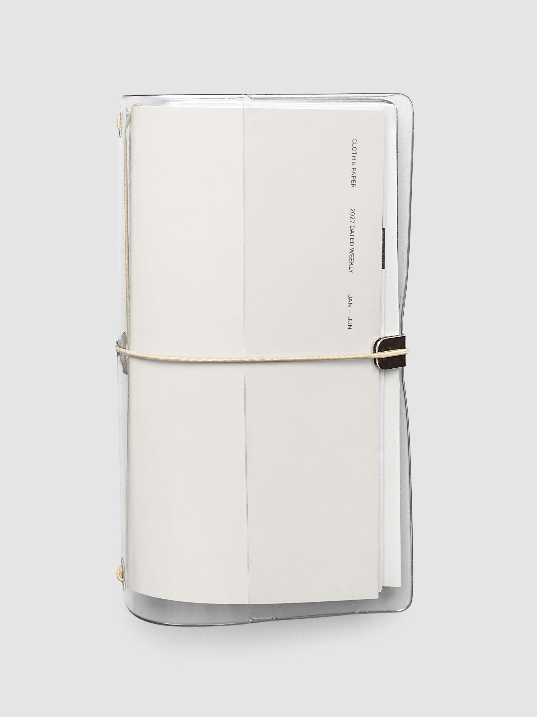 Closed clear vinyl travel notebook cover with a tan bungee cord and metal hardware, front page reading 2027 Dated Weekly January through June, A5 Slim size