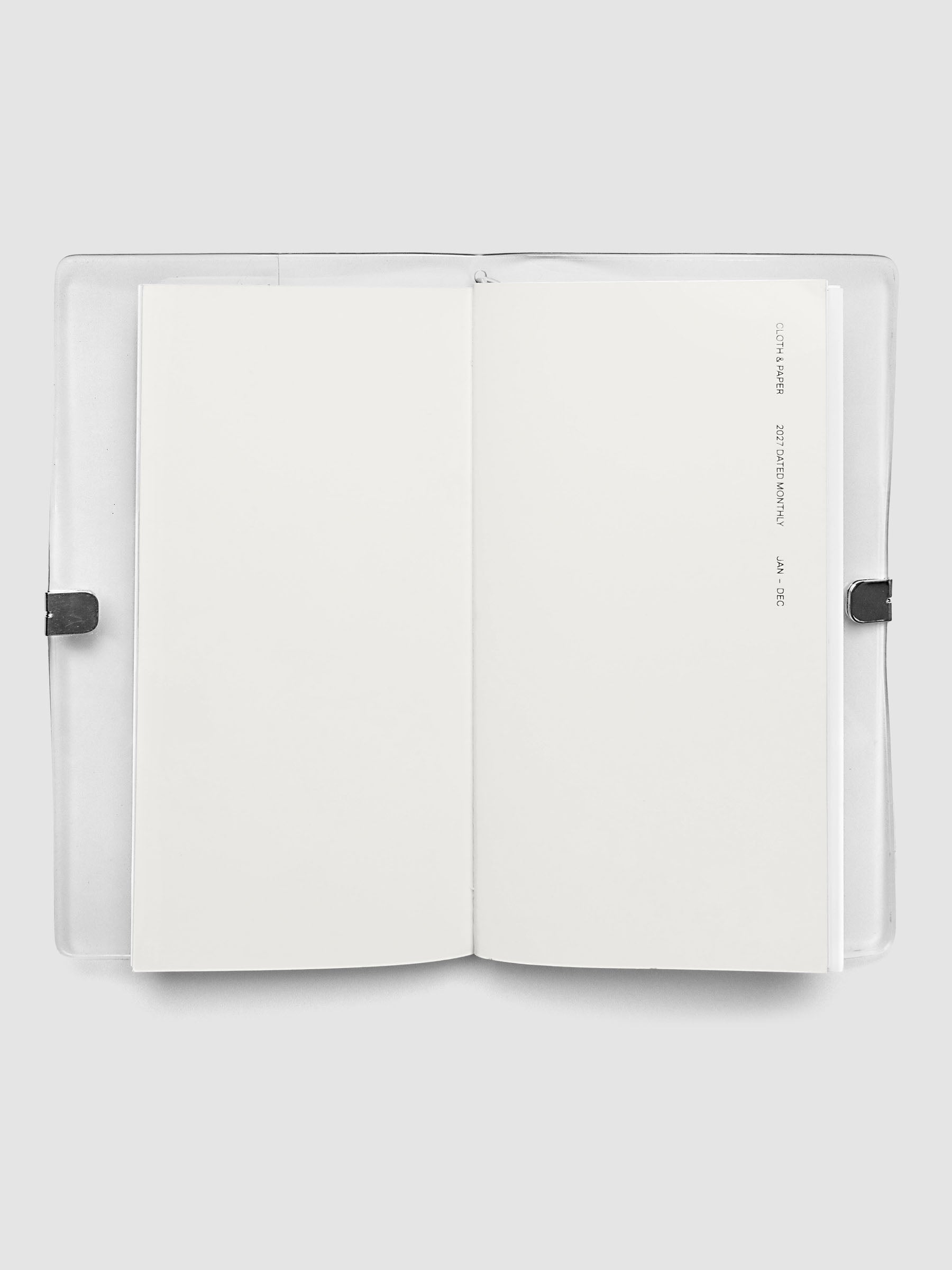 Open travel notebook showing a blank interior page, cover text reading 2027 Dated Monthly January through December, A5 Slim size