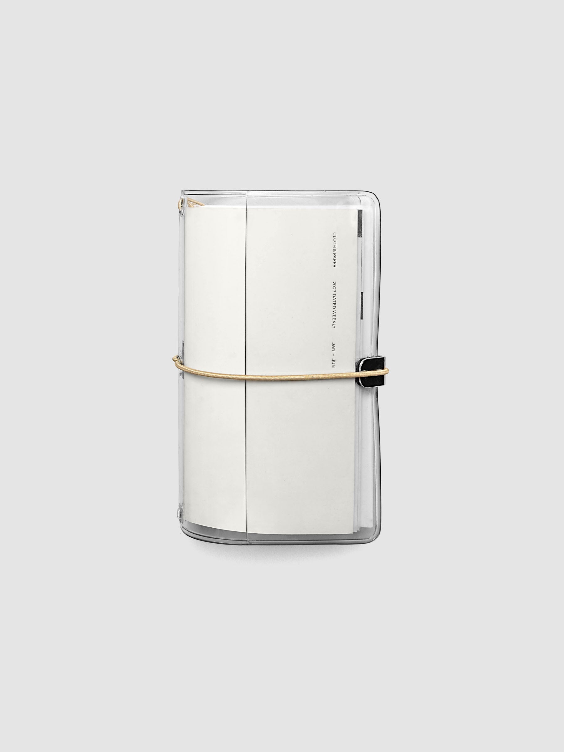 Closed clear vinyl travel notebook cover with a tan bungee cord and metal hardware, front page reading 2027 Dated Weekly January through June, Pocket Plus size