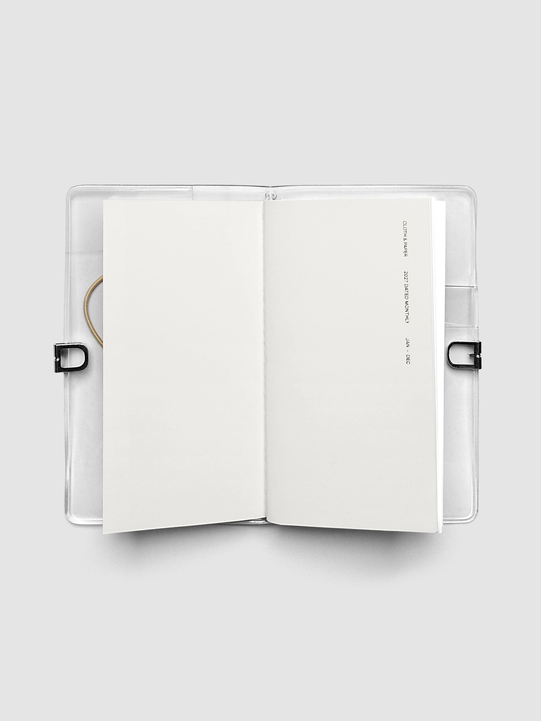 Open travel notebook showing a blank interior page, cover text reading 2027 Dated Monthly January through December, Pocket Plus size