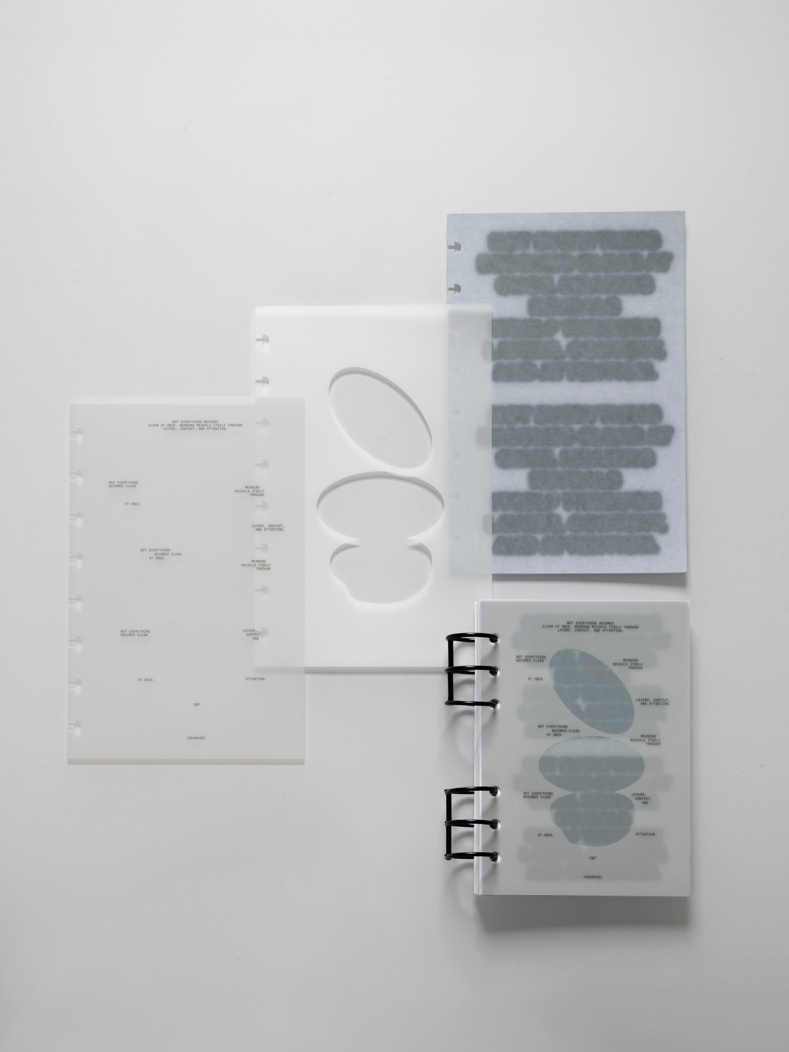 Frosted and vellum planner inserts laid flat on a light gray surface, including a printed text dashboard, an oval cutout dashboard, a gray marked sheet, and a ring bound notebook showing the pages layered together