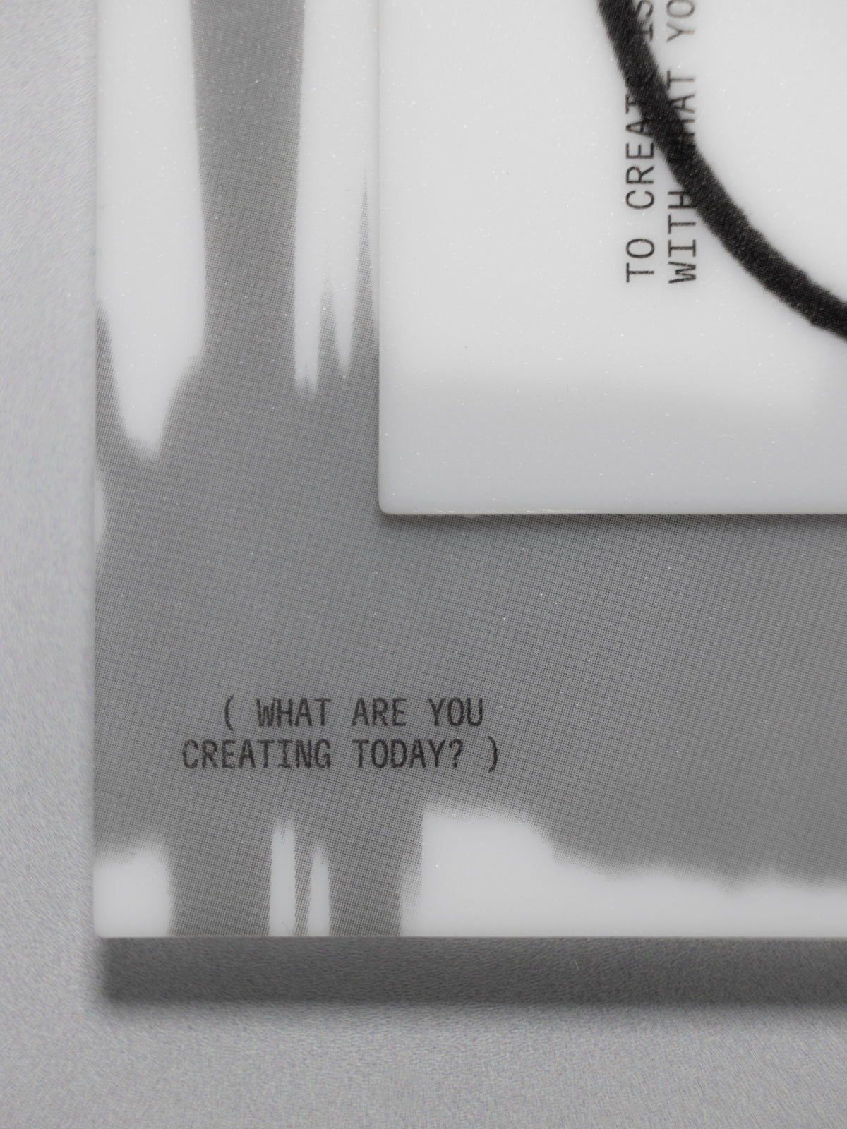 A close-up of a journaling card set with black printed text reading '( WHAT ARE YOU CREATING TODAY? )' and a black cord wrapped around the corner, shown against a gray background.