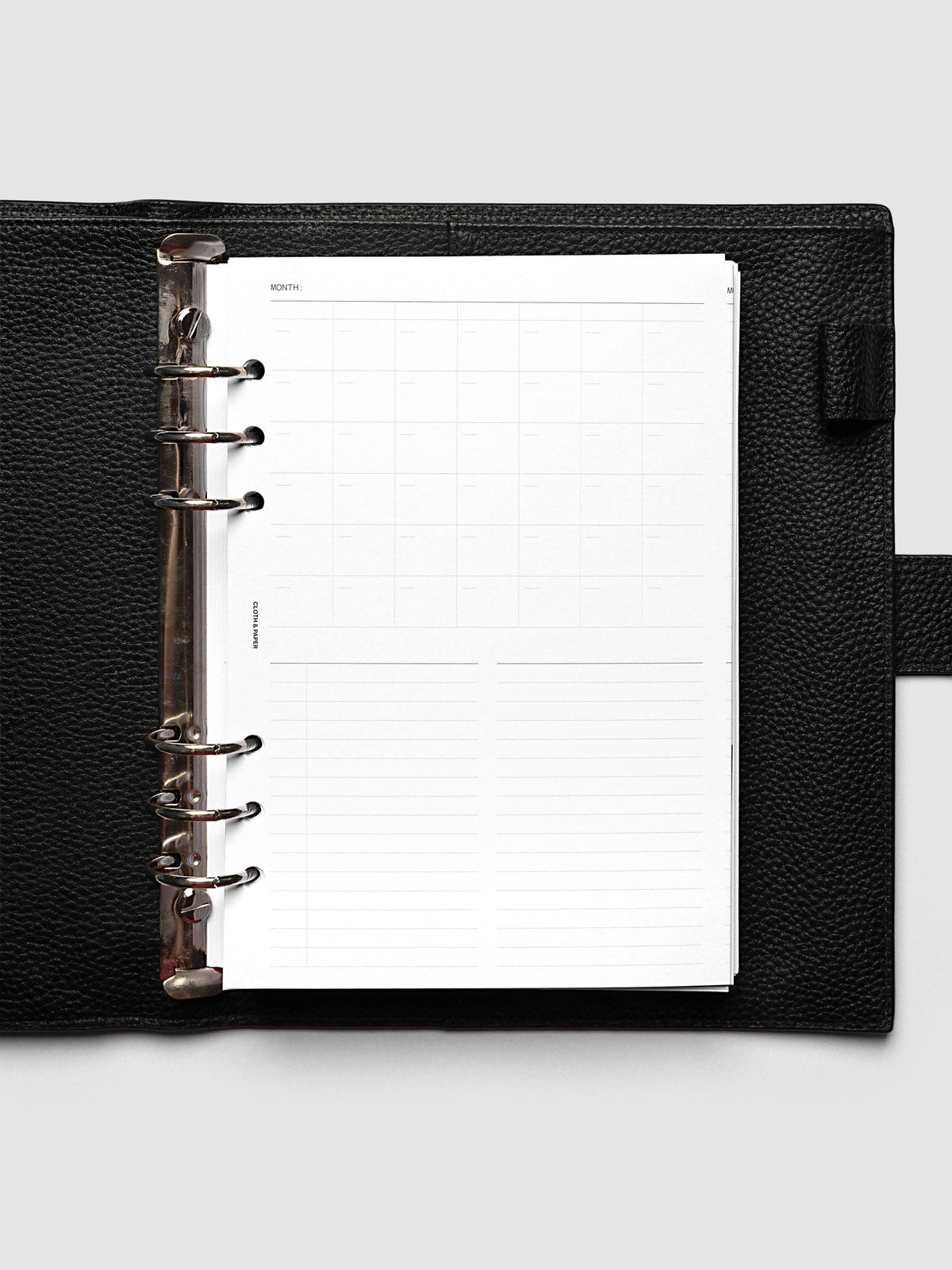 Monthly Fold Out Planner Insert Set of 2, A5 6-Ring Punch, the insert folded closed inside a black pebbled leather ring bound planner with silver rings, shot from directly above