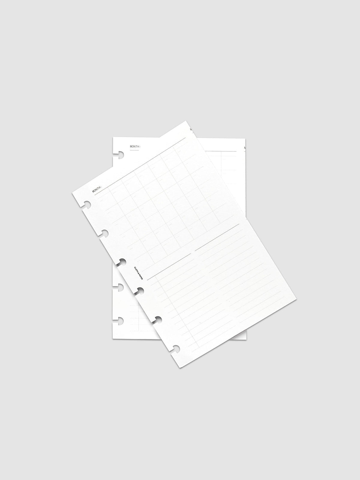 Monthly Fold Out Planner Insert Set of 2, CP Petite 6-Disc Punch, both inserts of the set layered at an angle on a pale gray surface, disc notches along the left edges