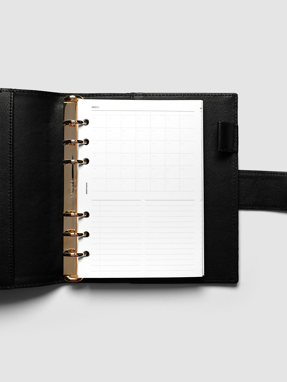 Monthly Fold Out Planner Insert Set of 2, Personal Wide 6-Ring Punch, the insert folded closed in a smooth black leather ring bound planner with gold rings and a wrap strap