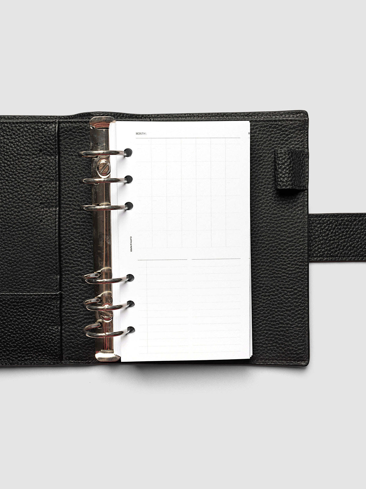 Monthly Fold Out Planner Insert Set of 2, Personal 6-Ring Punch, the insert folded closed in a black pebbled leather ring bound planner with silver rings and a wrap strap