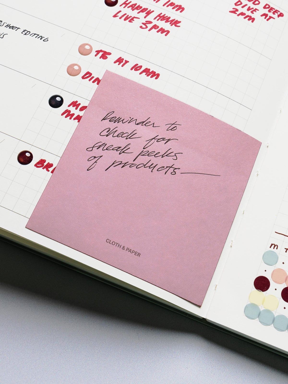 One pink/red sticky note in a planner with a reminder written in pen.