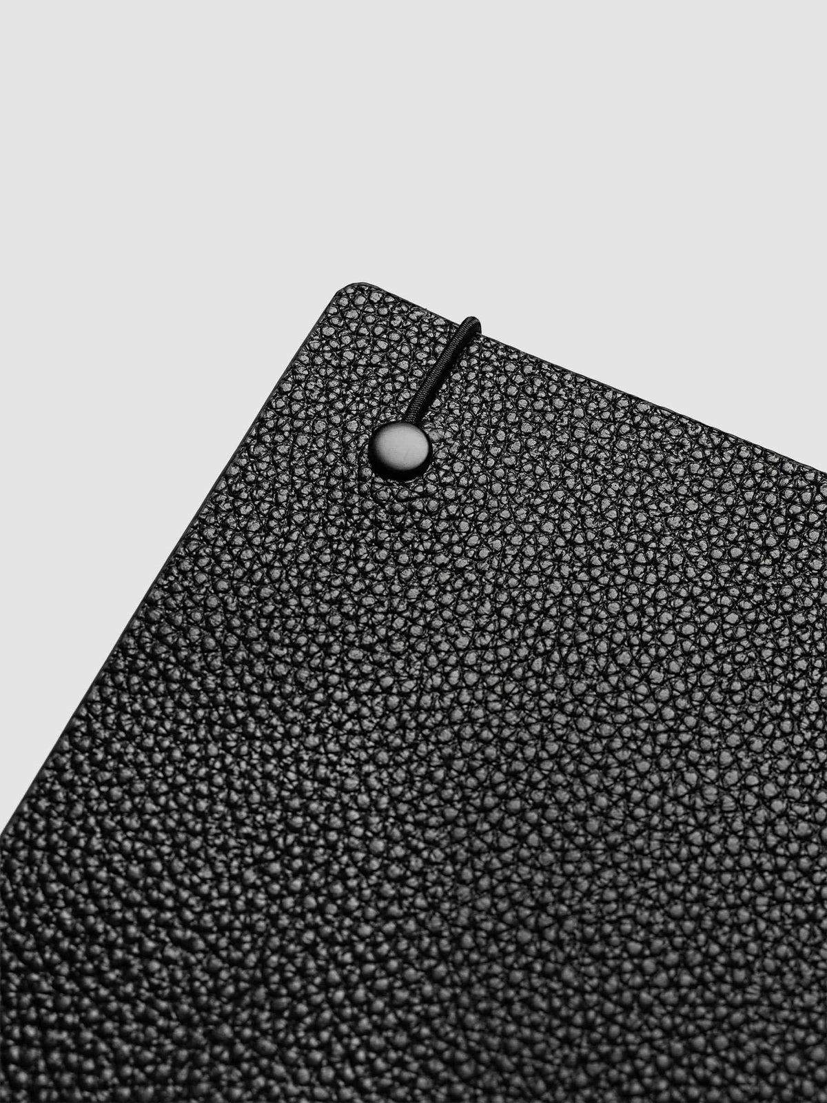 Close-up of the top corner of the A5 6-Ring Punch Genuine Leather Planner Cover Set, showing the bungee cord anchored to the black leather with a silver metal stud
