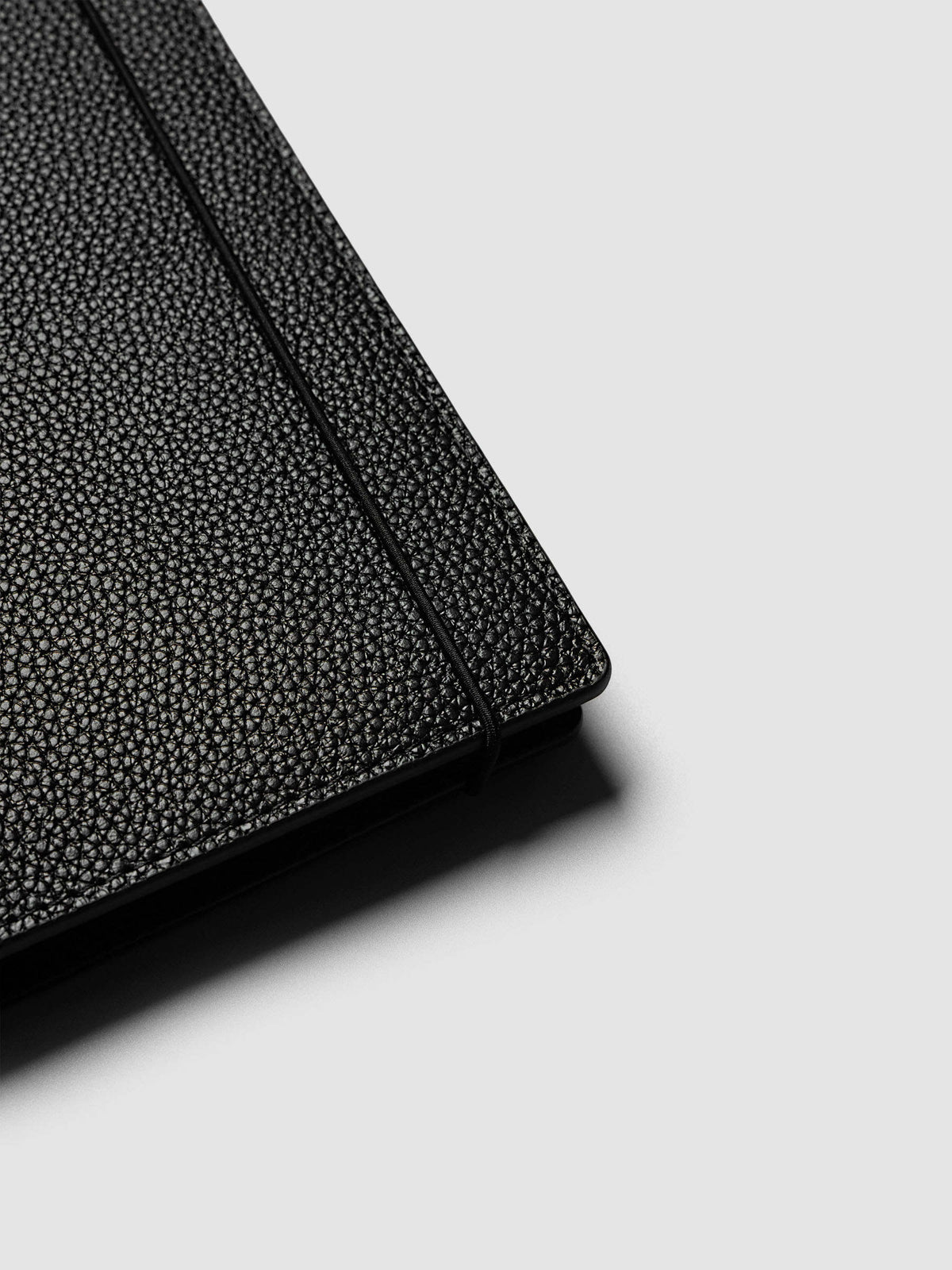Close-up of the corner of the A5 6-Ring Punch Genuine Leather Planner Cover Set with the bungee cord running along the edge of the pebbled black leather