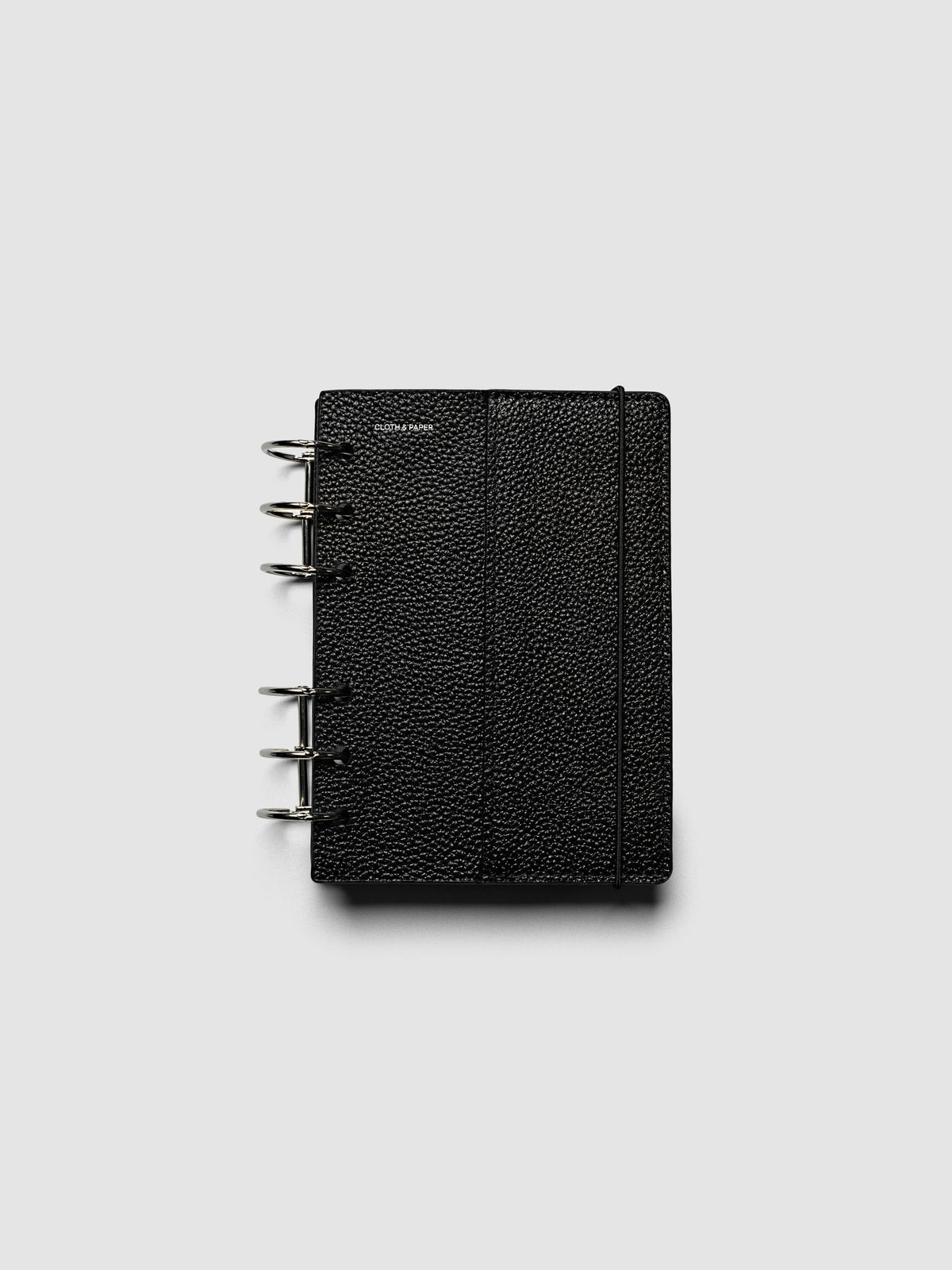 The A6 Genuine Leather Planner Cover Set closed on a ring bound planner, showing the silver rings, the silver foiled logo, and the bungee cord holding the stack shut