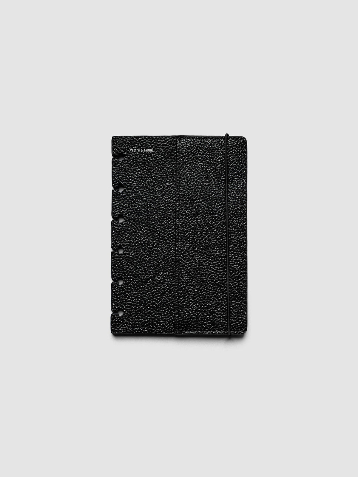 The front cover of the CP Petite 6-Disc Punch Genuine Leather Planner Cover Set laid flat, showing pebbled black leather, the silver foiled logo at the top left, the punch holes down the left edge, and the bungee cord running down the right