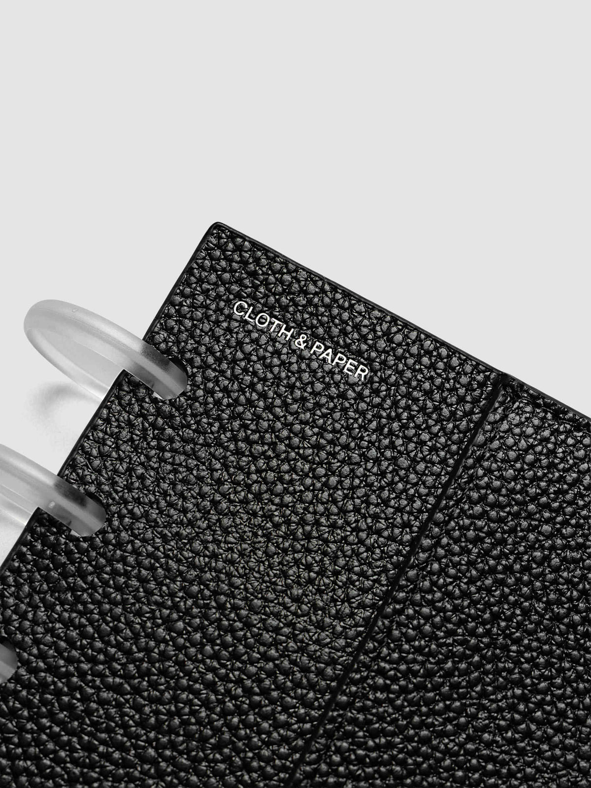 Close-up of the silver foiled Cloth and Paper logo on the pebbled black leather front cover of the Half Letter 8-Disc Punch Genuine Leather Planner Cover Set