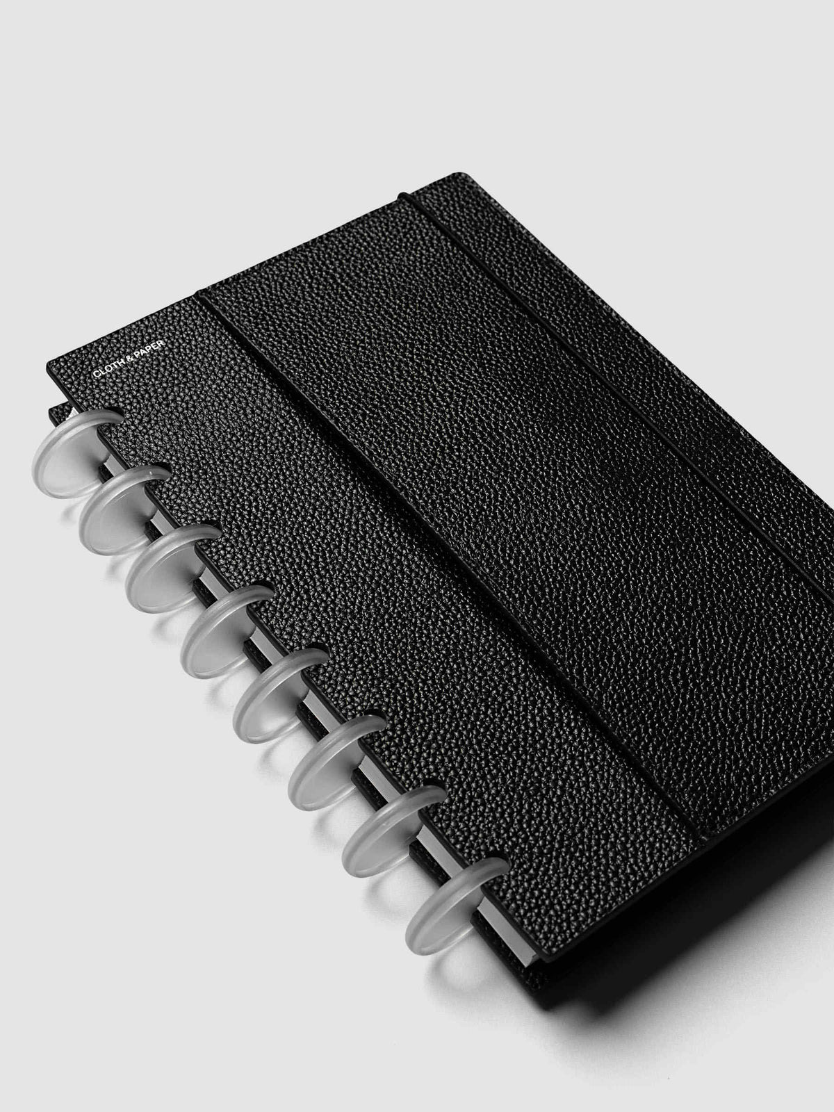Close-up of the top corner of the Half Letter 8-Disc Punch Genuine Leather Planner Cover Set, showing the bungee cord anchored to the black leather with a silver metal stud