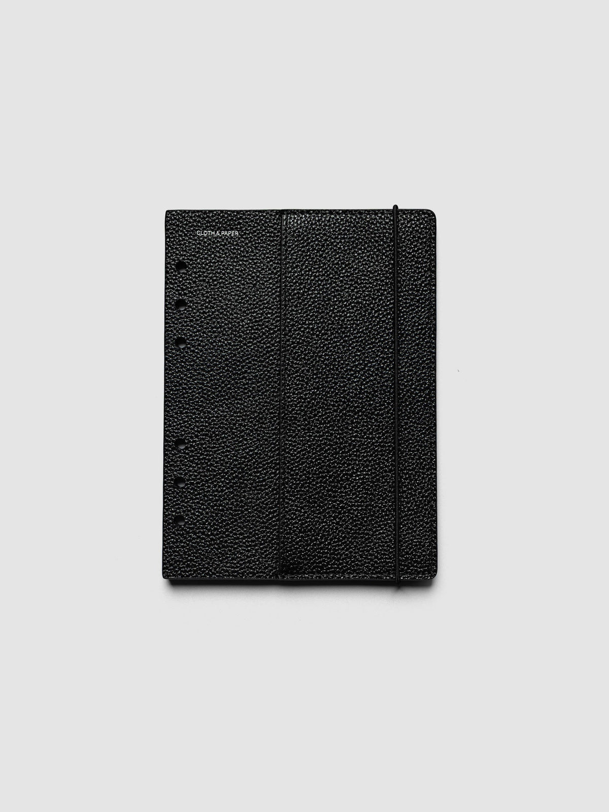 The front cover of the Personal Wide Genuine Leather Planner Cover Set laid flat, showing pebbled black leather, the silver foiled logo at the top left, the punch holes down the left edge, and the bungee cord running down the right