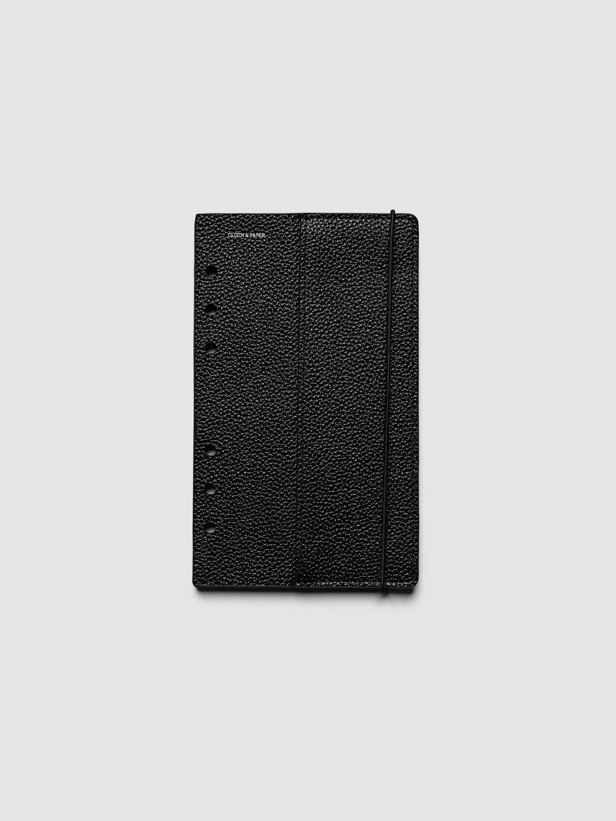 The front cover of the Personal Genuine Leather Planner Cover Set laid flat, showing pebbled black leather, the silver foiled logo at the top left, the punch holes down the left edge, and the bungee cord running down the right