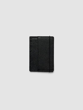 The front cover of the Pocket Genuine Leather Planner Cover Set laid flat, showing pebbled black leather, the silver foiled logo at the top left, the punch holes down the left edge, and the bungee cord running down the right
