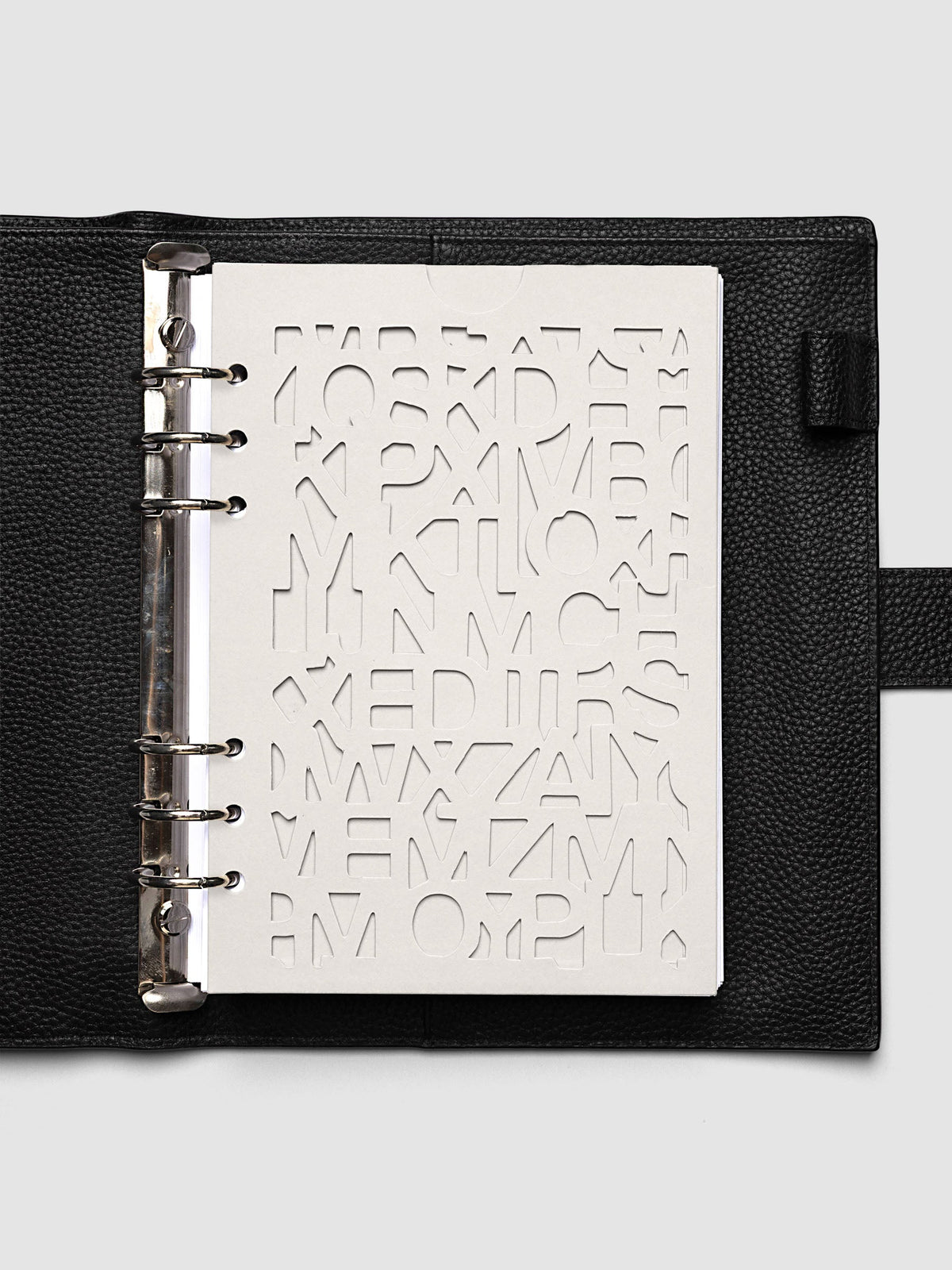 The A5 6-Ring Punch Diecut Pocket Folder empty at the front of a black leather ring bound planner, the cut letters showing the blank page beneath