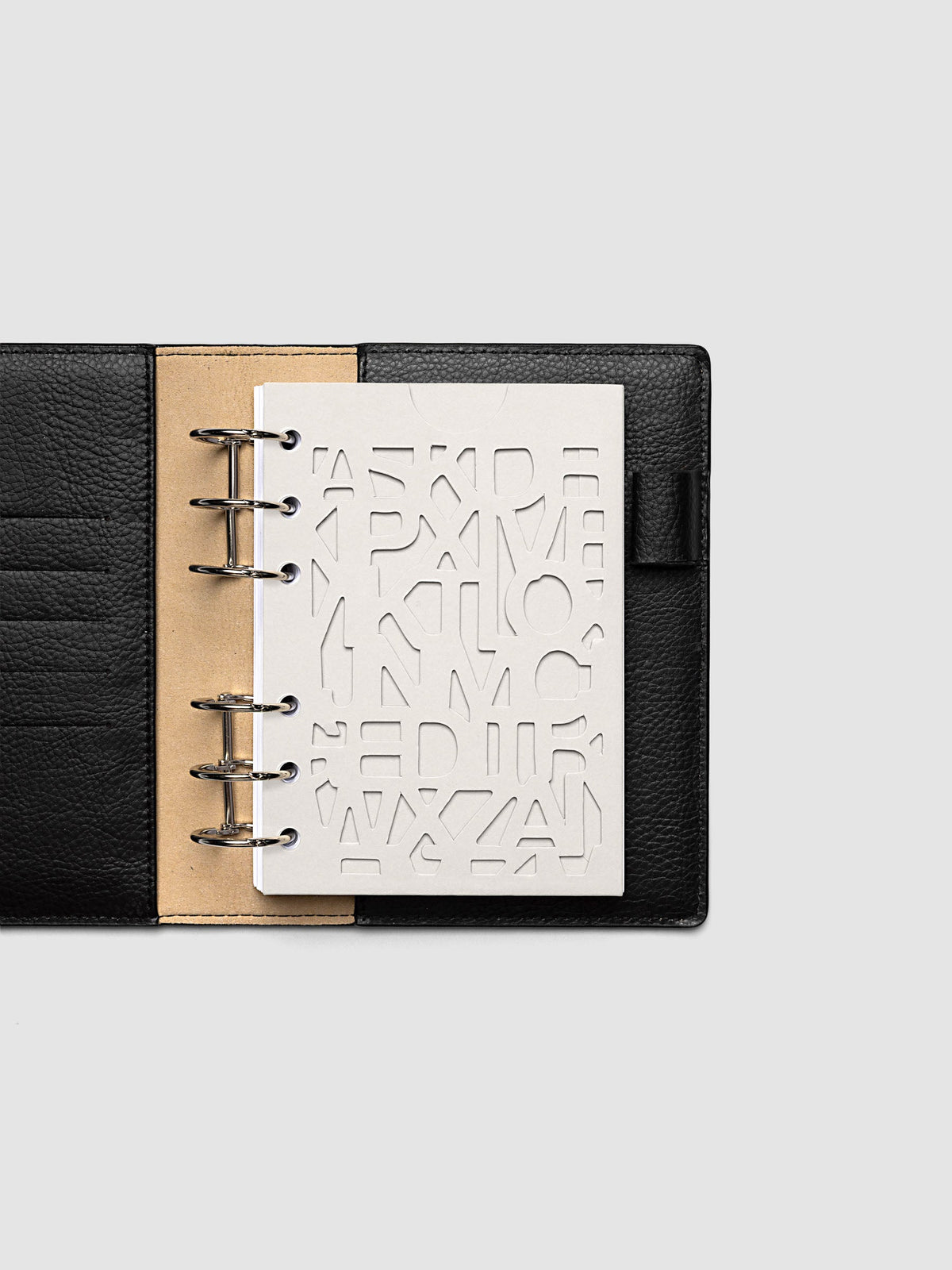 The A6 Diecut Pocket Folder empty at the front of a black leather ring bound planner, the cut letters showing the blank page beneath